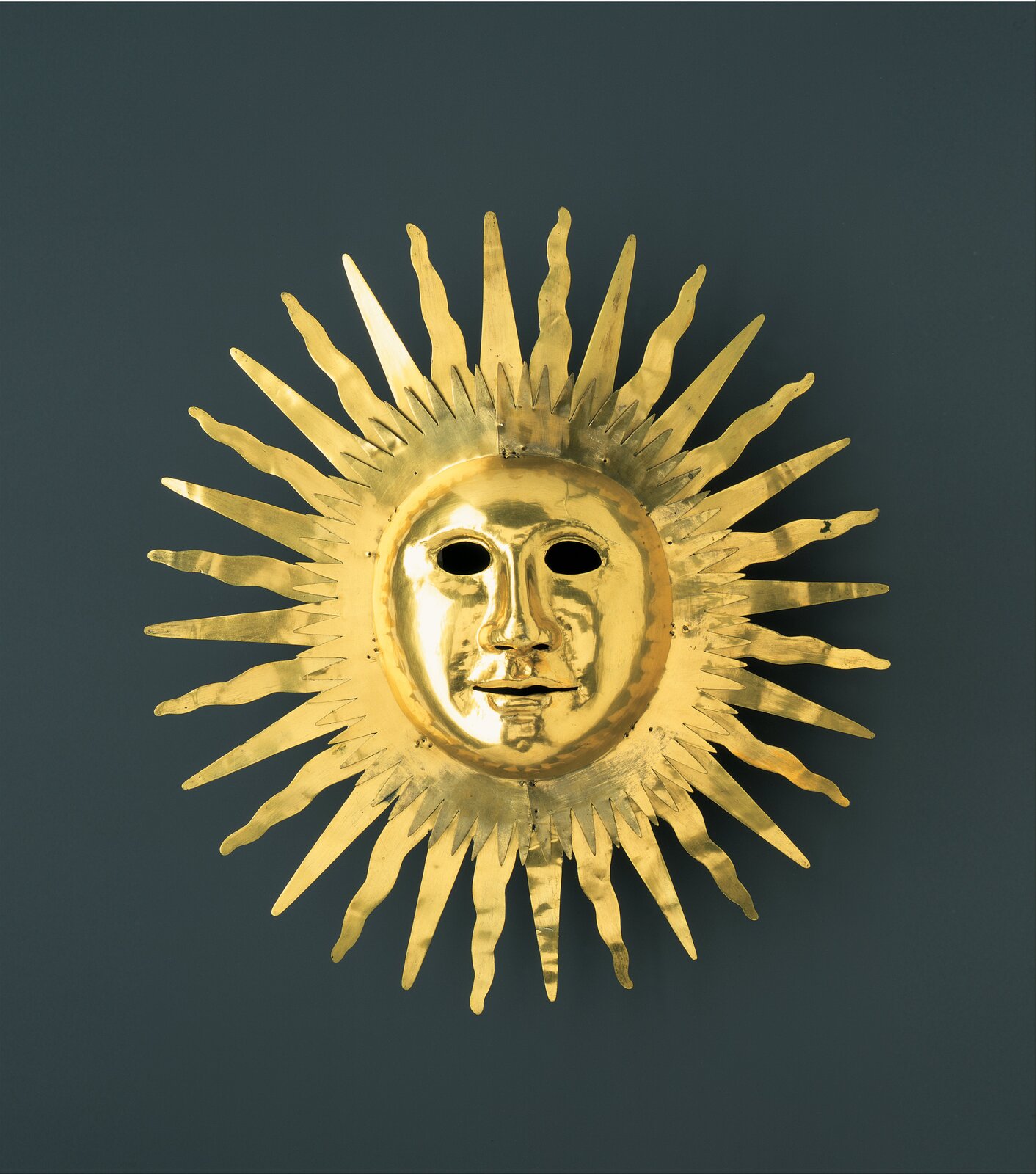 Fotografia przedstawia maskę w kształcie Słońca z rysami twarzy Augusta II Mocnego jako Apolla. Maska jest zrobiona ze złota.