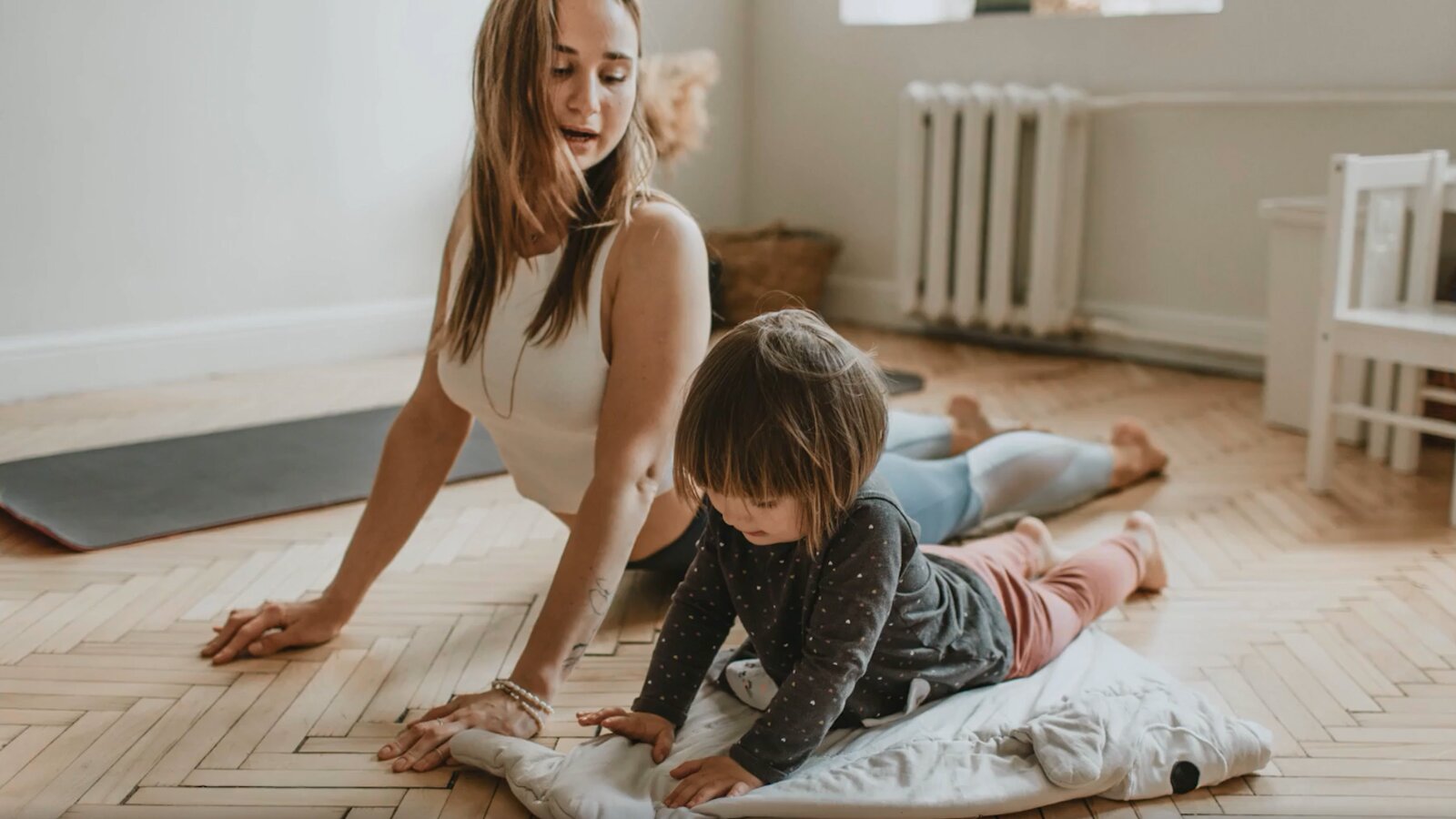 Ilustracja przedstawia młodą kobietę i kilkuletnie dziecko podczas wykonywania ćwiczeń jogi.