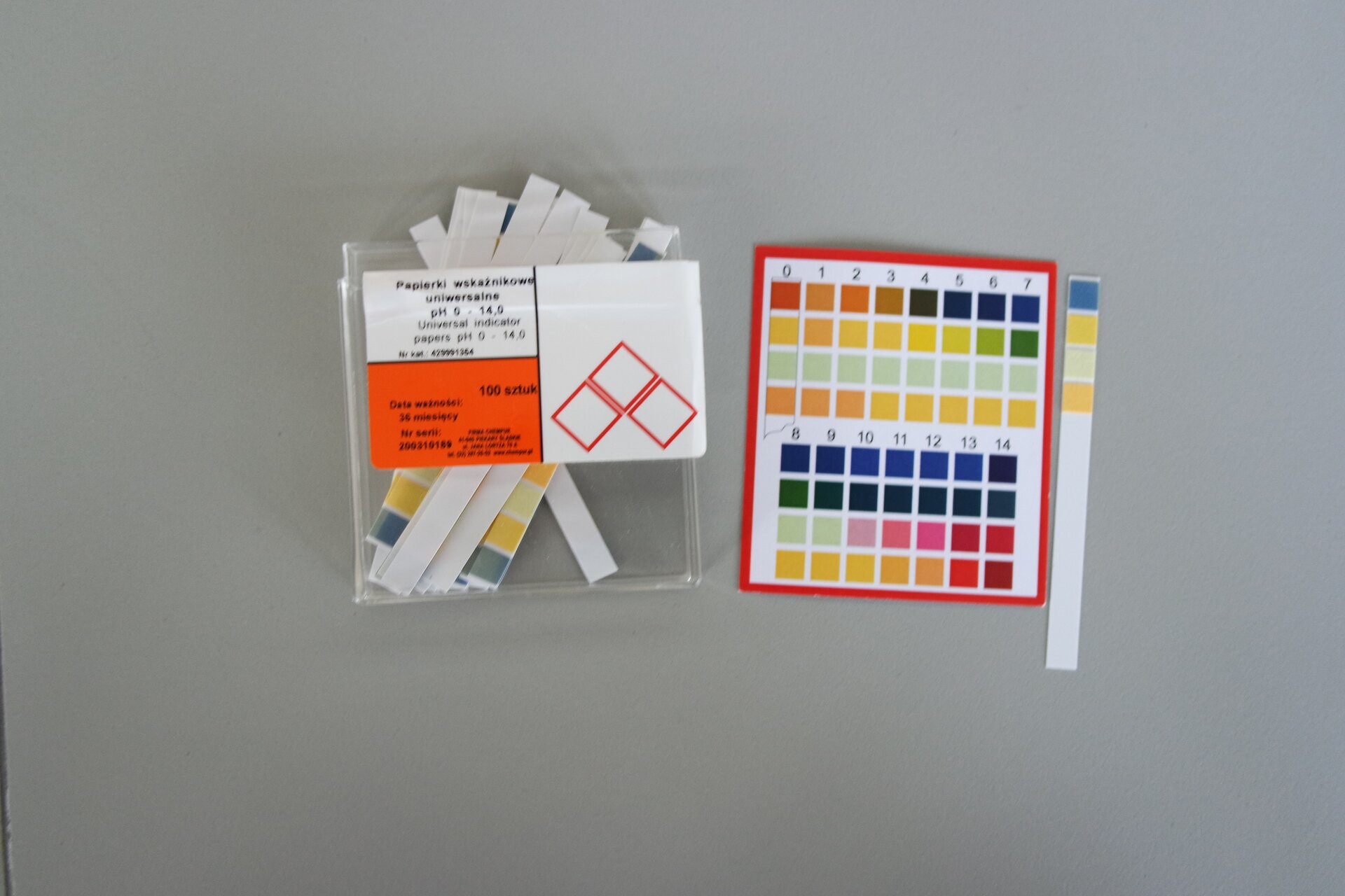 Zdjęcie prezentuje papierki lakmusowe do oznaczania pH. To różnokolorowe papierki umieszczone w foliowej torebce; tuż obok widoczna jest numeryczna tabela ze skalą barw.