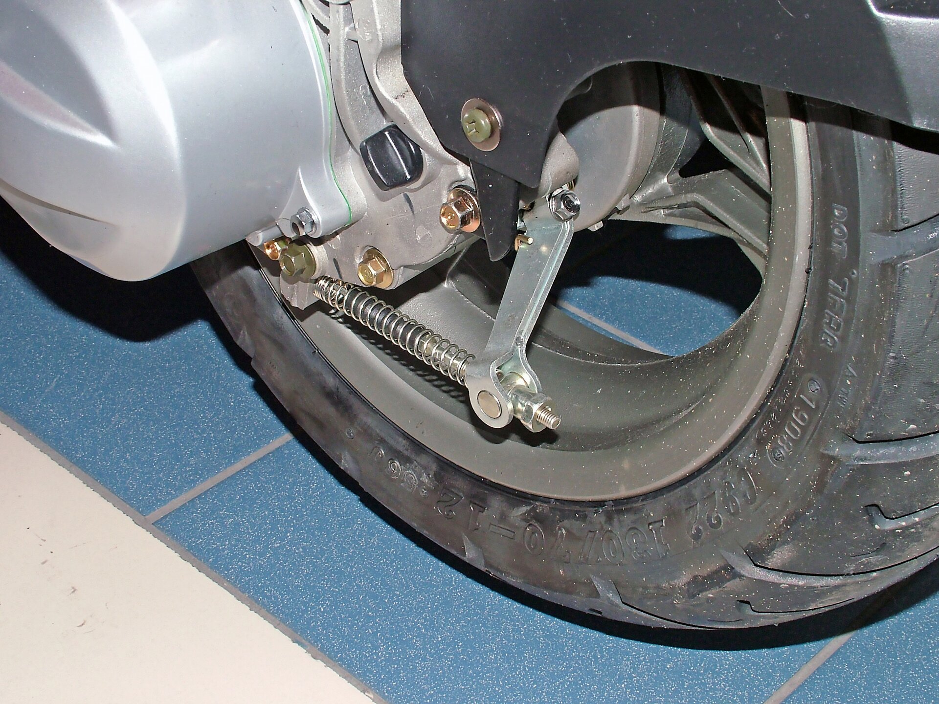 Na ekranie przedstawiona jest opona pojazdu, a dokładniej zbliżenie na korek spustowy oleju silnikowego głęboko ukryty pomiędzy kolektorami wylotowymi.