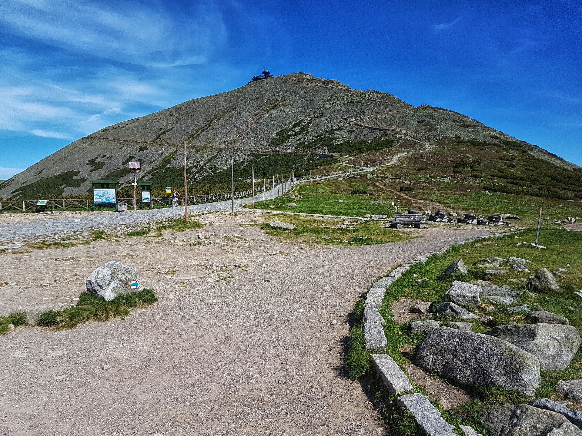 Zdjęcie przedstawia szlak turystyczny wiodący na Śnieżkę w Karkonoszach. Szczyt jest stosunkowo łagodny. Zbocza Śnieżki pokrywa gołoborze. Na szczycie stoi restauracja i obserwatorium. 