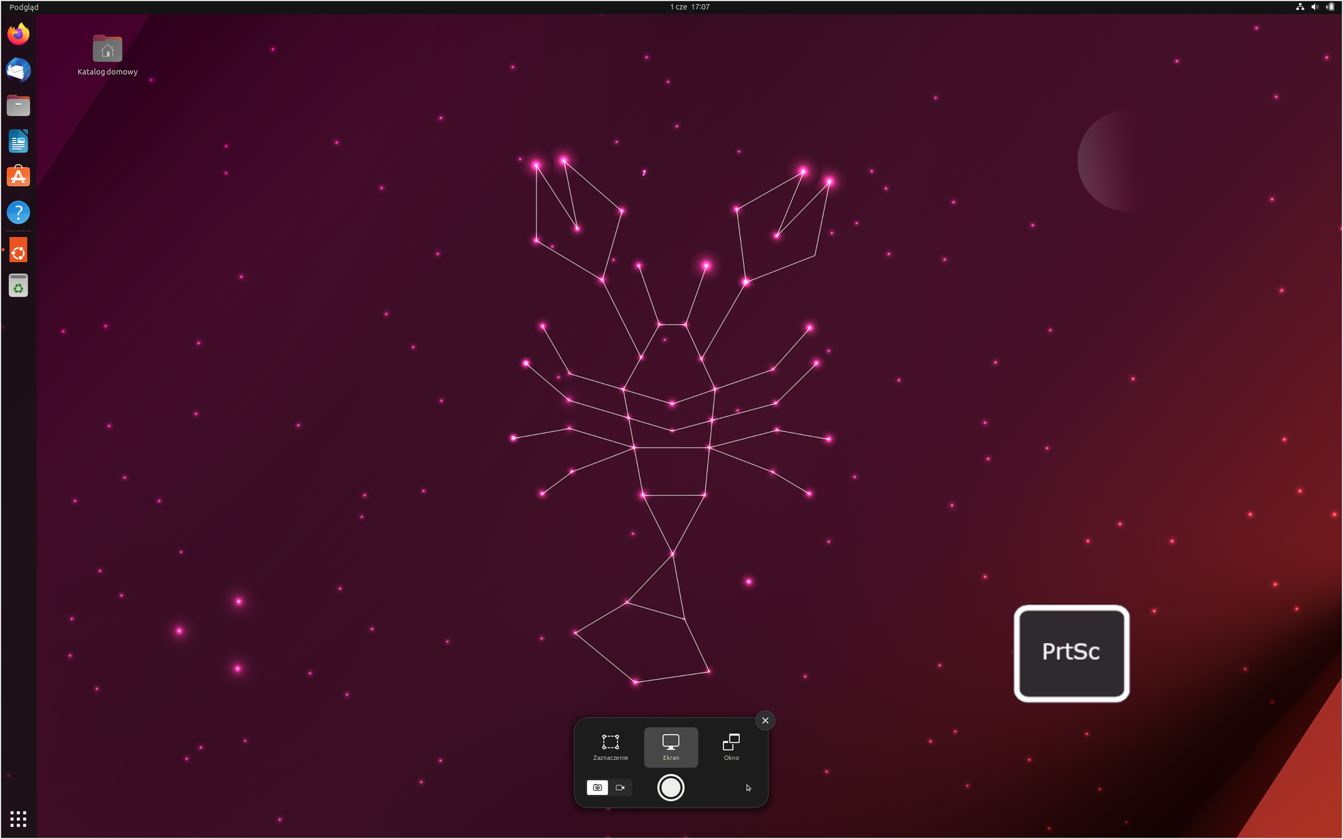 Ilustracja przedstawia pulpit Ubuntu w wersji 23.04. Na tapecie znajduje się homar złożony z figur geometrycznych. W lewym górnym rogu znajduje się ikona folderu katalogu domowego. Na pulpicie umieszczono grafikę przedstawiającą klawisz PrtSc.