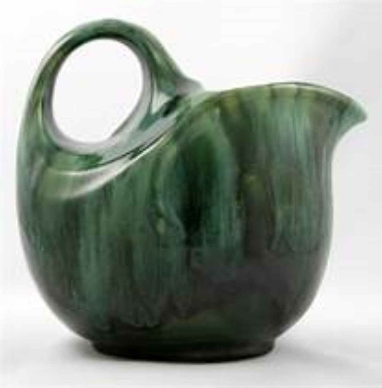 Fotografia przedstawia ceramiczny dzbanek w odcieniu zieleni. Ma pękaty kształt, owalne ucho z lewej strony, dzióbek z prawej. Kolor na wazonie układa się pionowymi, nieregularnymi smugami od jasnej, do ciemnej zieleni.