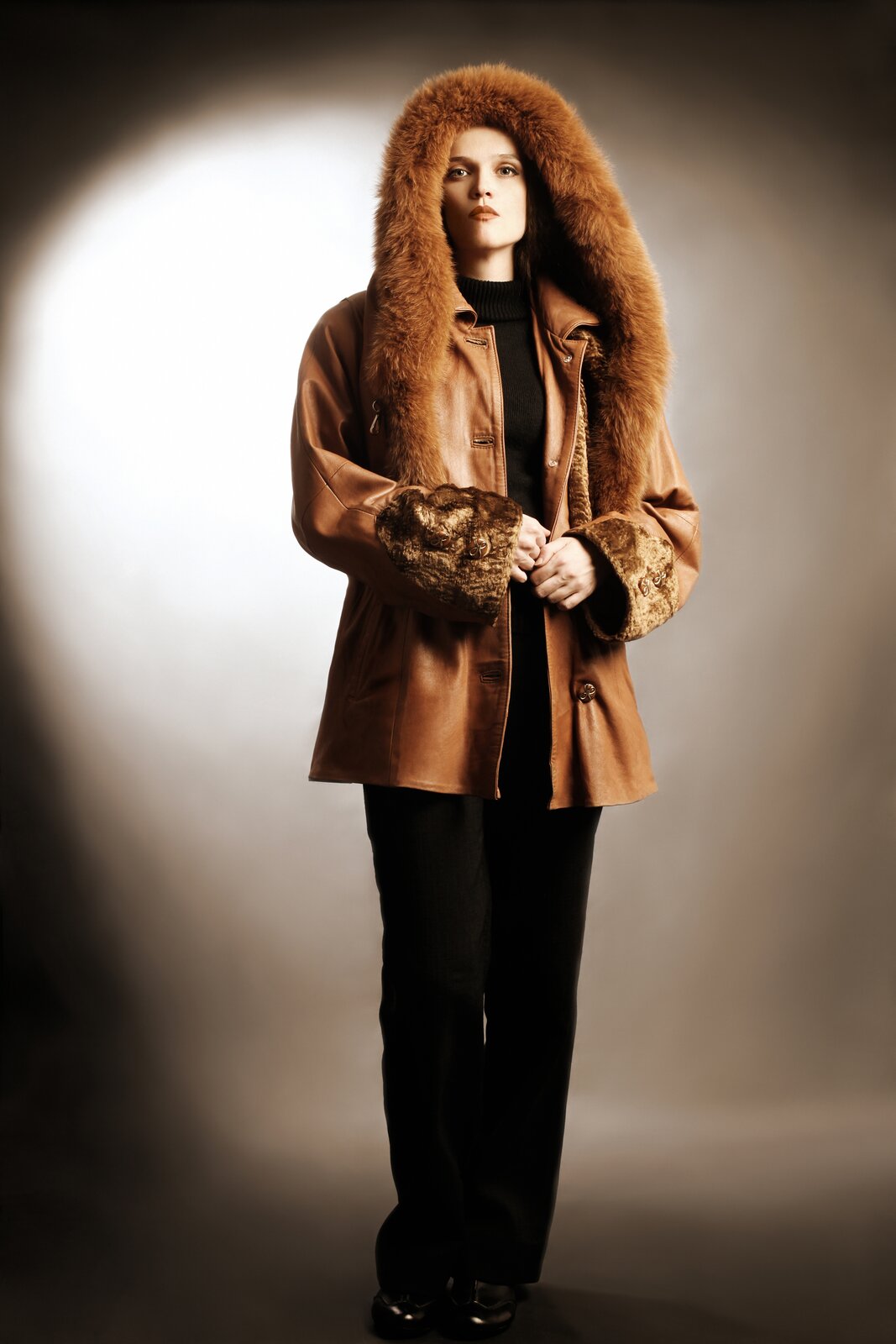 Na zdjęciu widoczna krótka kurtka w ciemnobeżowym kolorze, błyszcząca, z czarnym zamkiem i kieszeniami. Dół kurtki, kołnierz oraz dół rękawów są obszyte futrem w tym samym kolorze. Nagranie tożsame z treścią.