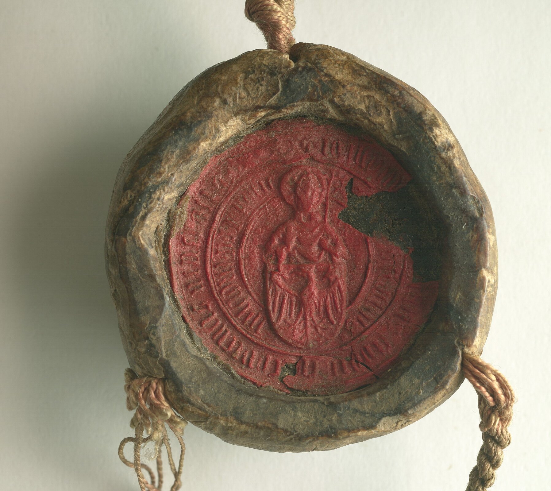 Zdjęcie przedstawia okrągłą pieczęć lakową, na której widnieje odbita postać świętego z pastorałem w ręku i orłem u swoich stóp. 