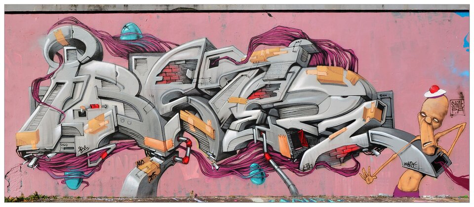 Zdjęcie przedstawia graffiti namalowane na różowej ścianie. Graffiti ukazuje szary napis wzbogacony innymi elementami graficznymi, z prawej strony znajduje się postać łysego, półnagiego mężczyzny z beretem na głowie.