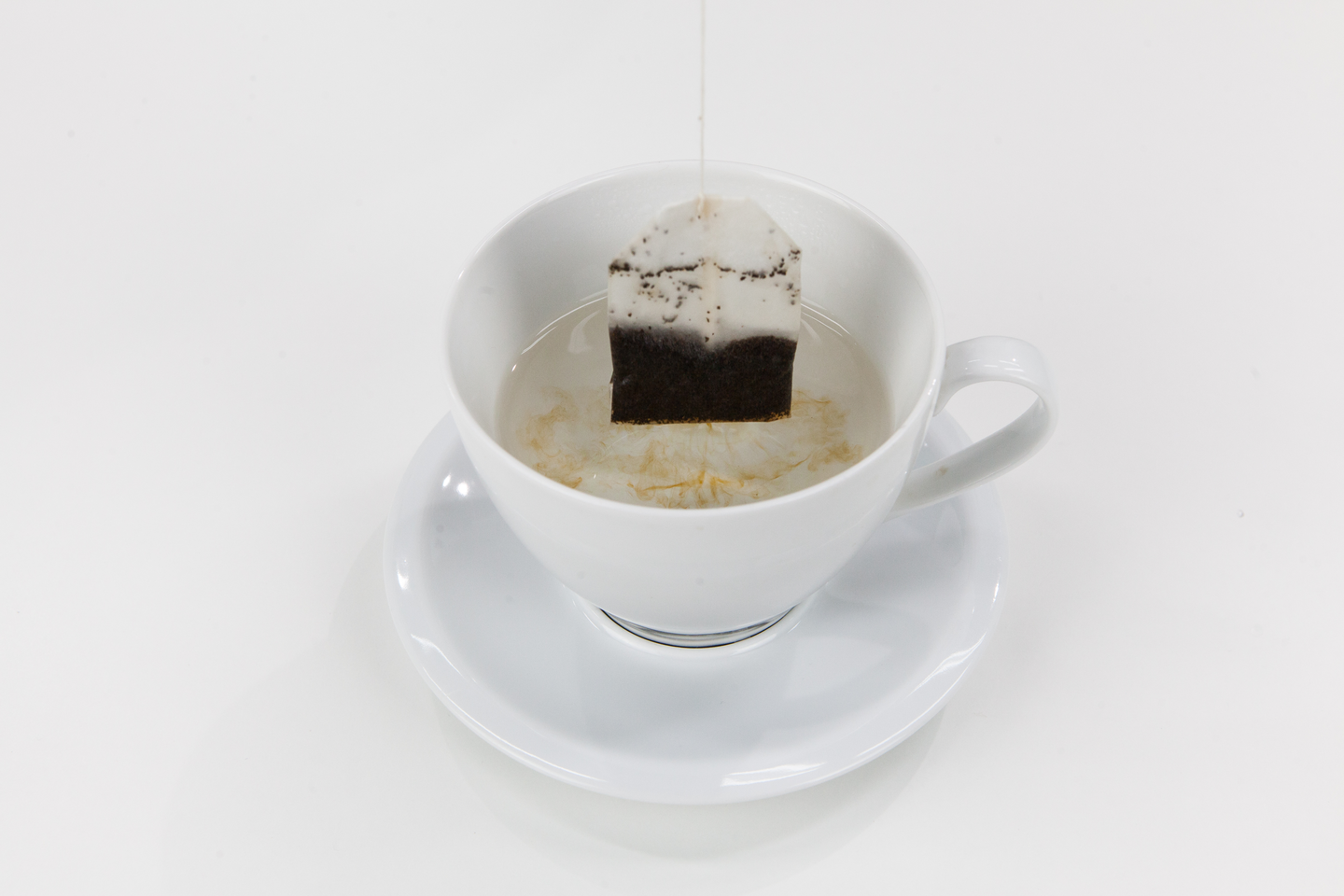 Fotografia przedstawia torebkę herbaty zanurzonej w filiżance. Woda zaczyna zabarwiać się kolorem herbaty.  