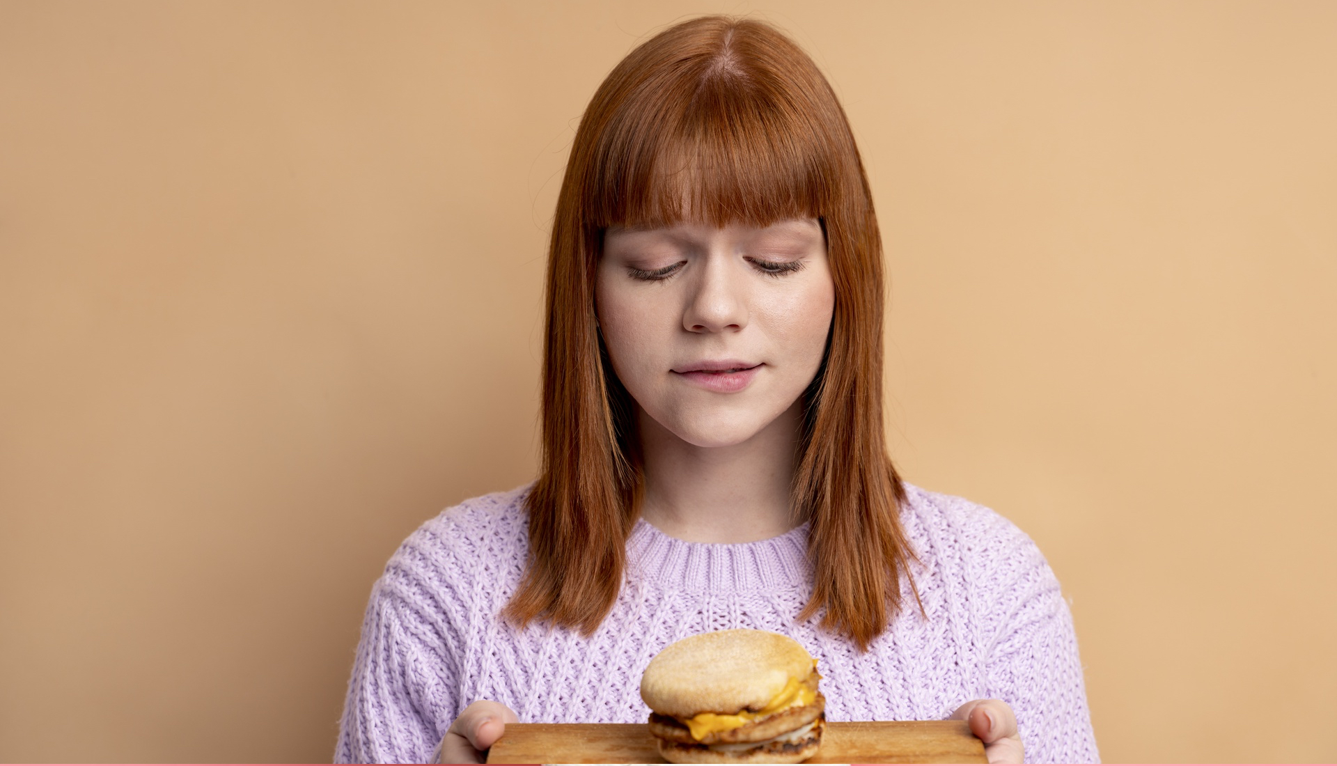 Zdjęcie przedstawia nastolatkę trzymającą w dłoniach przed sobą deskę, na której leży hamburger. 