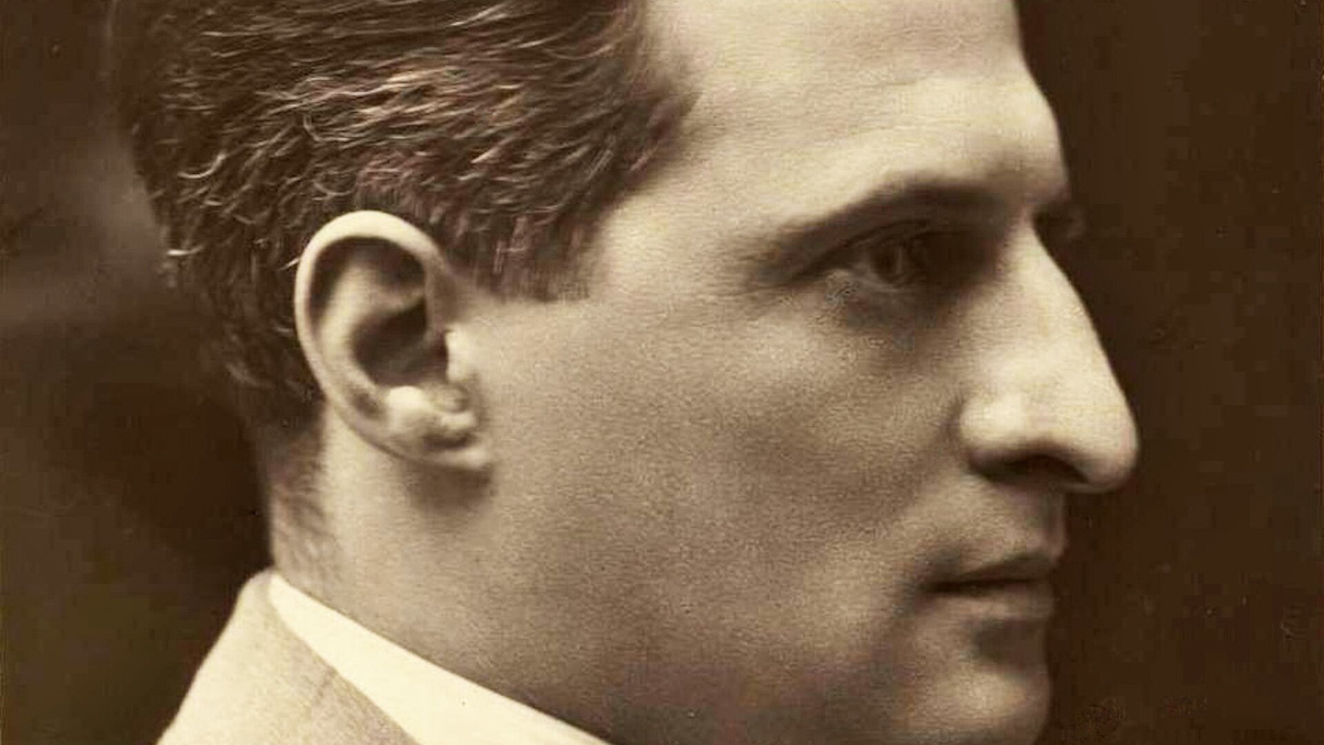 Zdjęcie przedstawia prawy profil młodego mężczyzny. Ma krótko przystrzyżone włosy, wysokie czoło i wydatny nos.