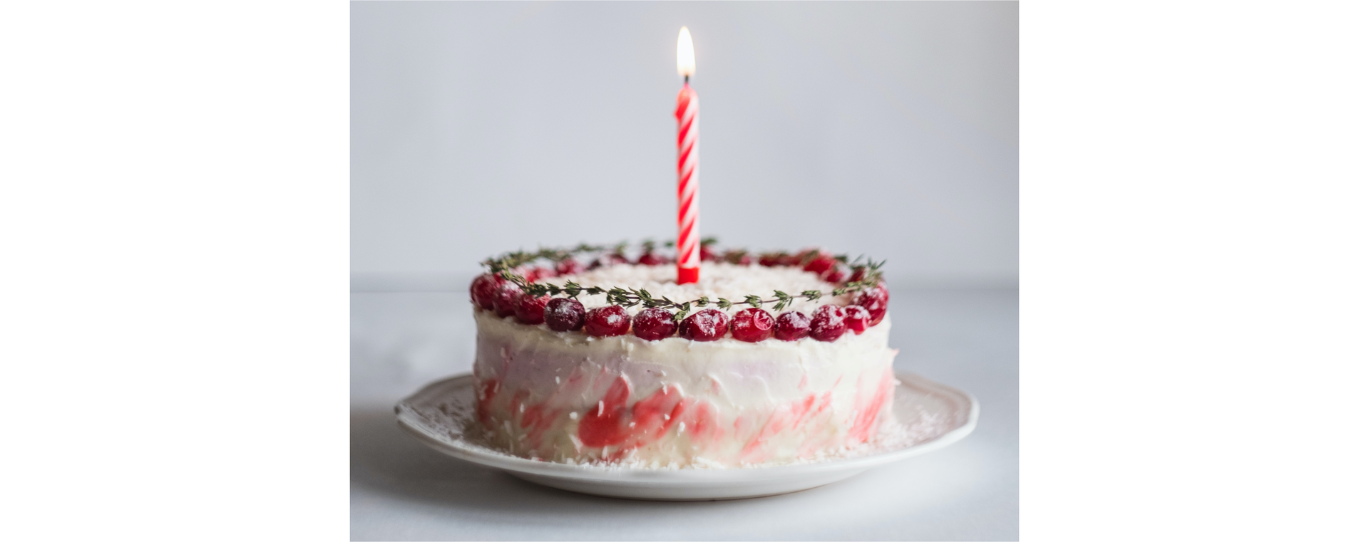 Zdjęcie przedstawia tort urodzinowy z owocami na wierzchu. Tort znajduje się na talerzu. Na torcie zapalona jest jedna świeczka.