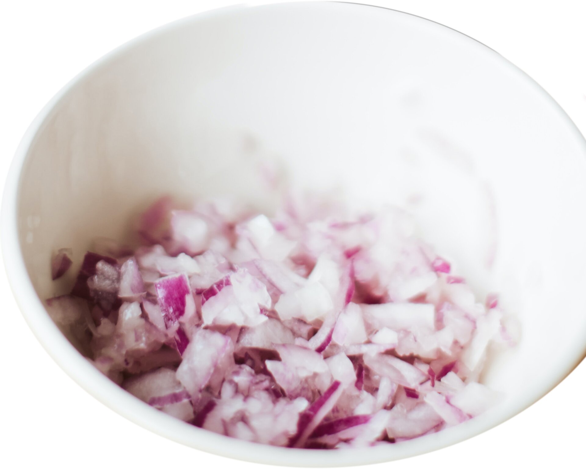 Zdjęcie przedstawia czerwoną cebulę pokrojoną techniką mirepoix. Widoczne są nieregularne  i różnej wielkości fragmenty czerwonej cebuli w niewielkiej białej miseczce pokazanej w ujęciu z góry.