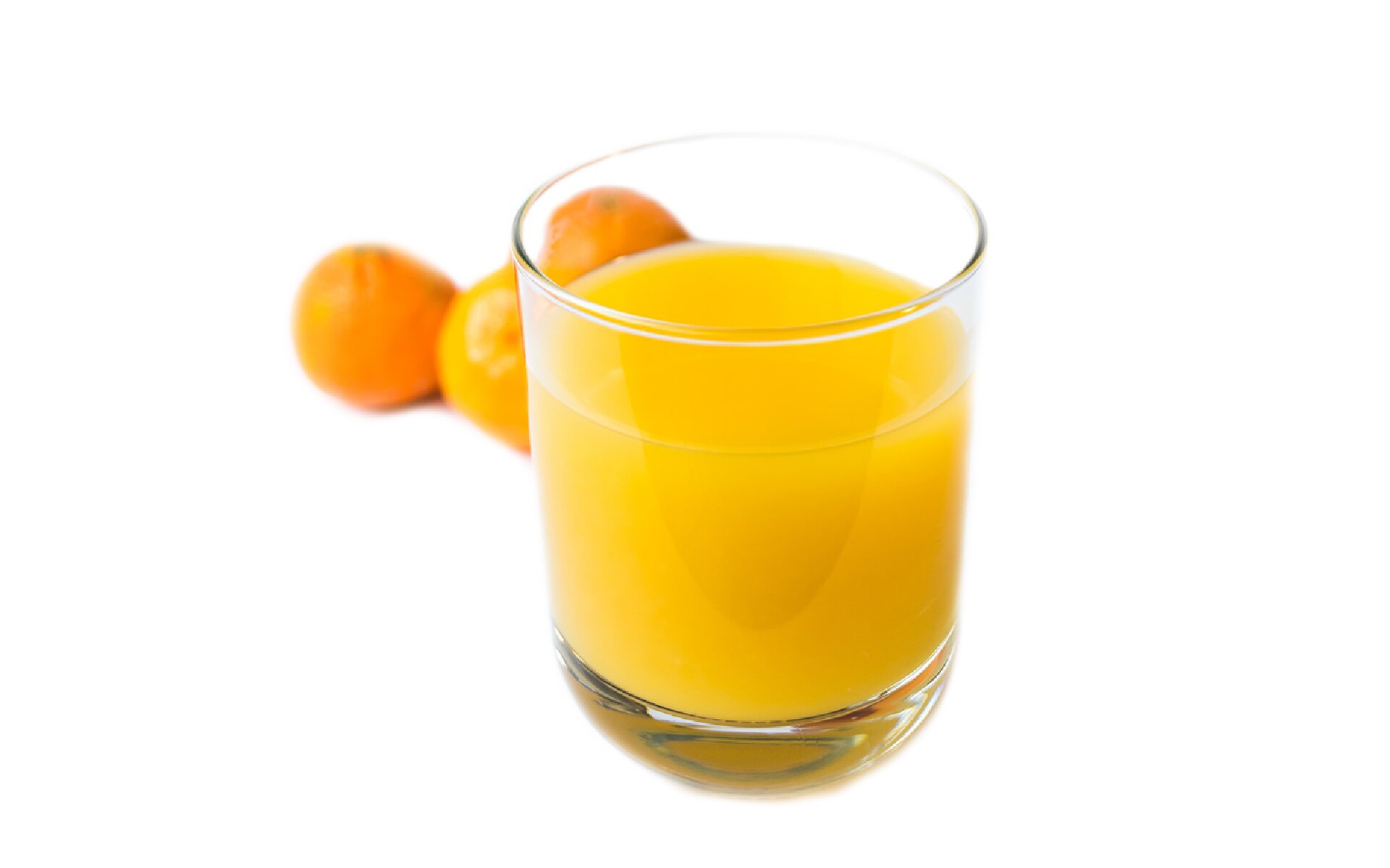 Zdjęcie przedstawia szklankę z sokiem na pierwszym planie, a za nią pomarańcze. 