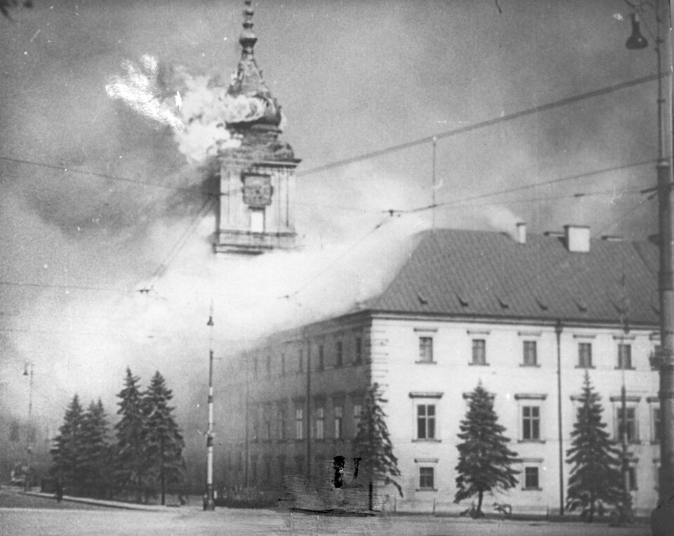 Zdjęcie przedstawia pożar Zamku Królewskiego. Otwarty ogień wydobywa się z wieży zamkowej nad zegarem.