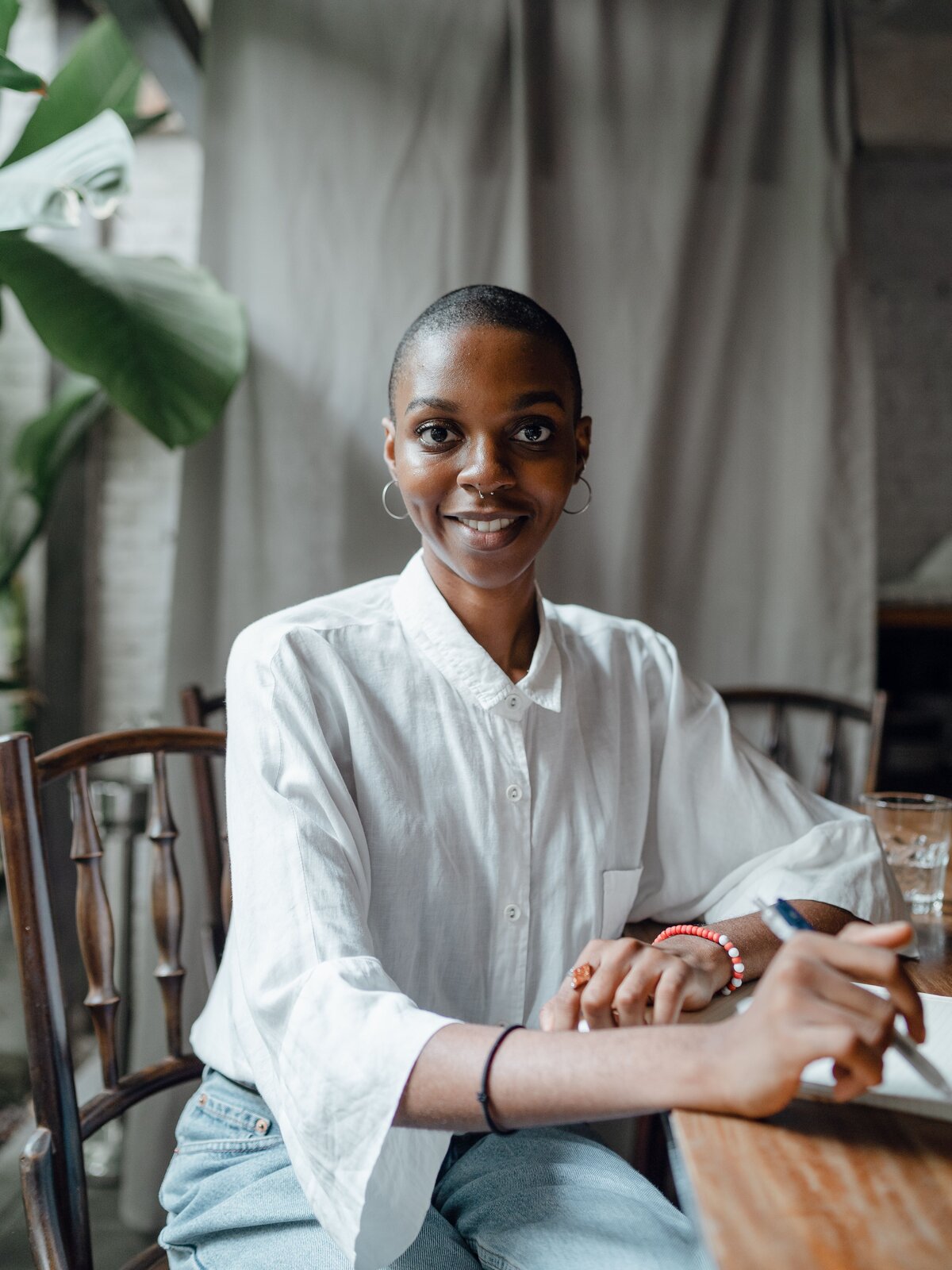 Zdjęcie przedstawia młodą kobietę ubraną w elegancką białą bluzkę z rozszerzonym rękawami i jasno niebieskimi jeansami. 