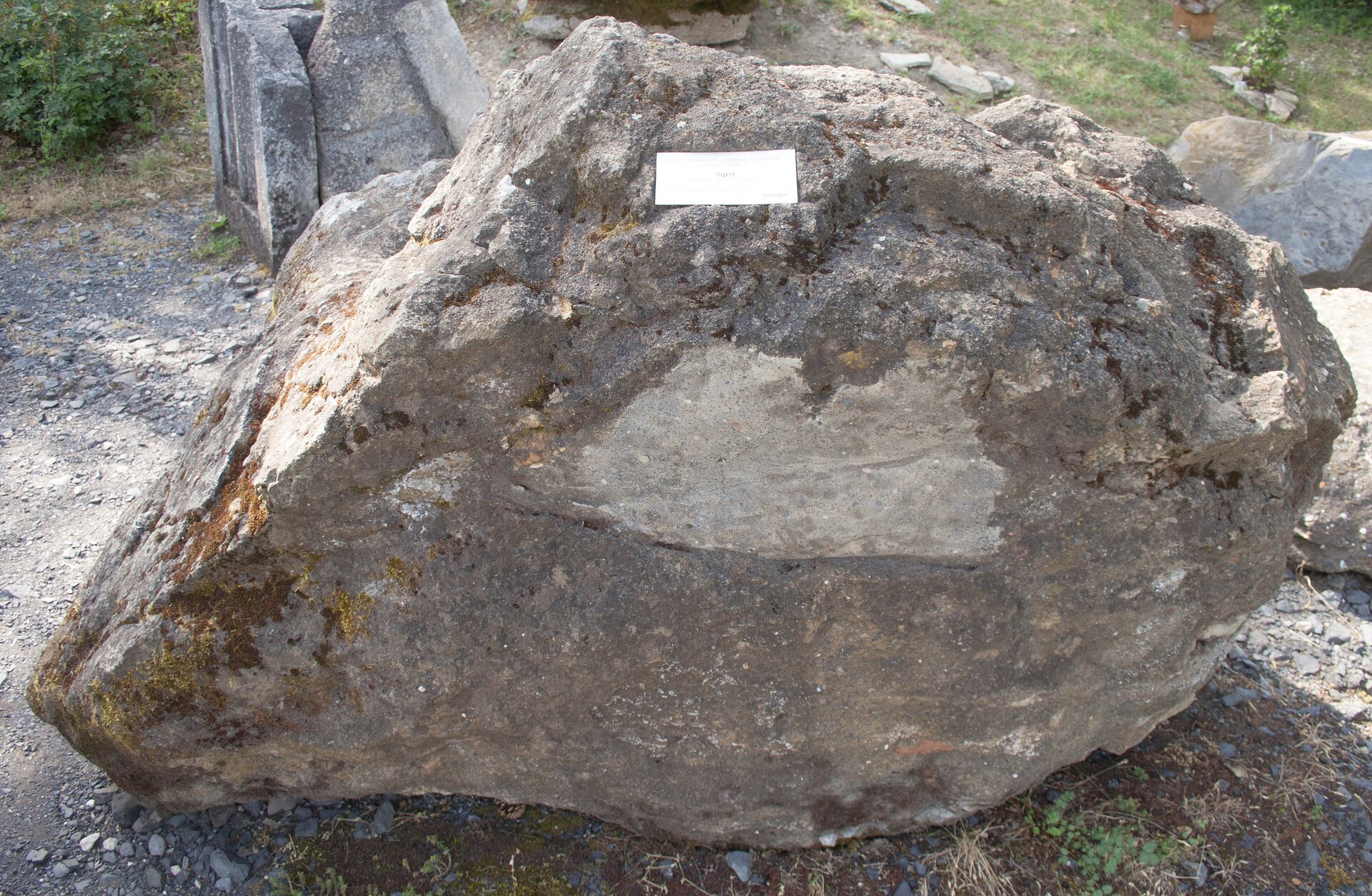 Zdjęcie przedstawia tifit. Jest to stosunkowo duża skała o chropowatej powierzchni i o szarej barwie. Znajduje się na niej mech.