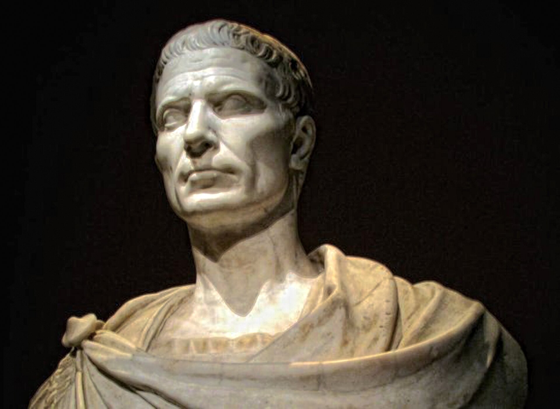Ilustracja przedstawia popiersie Juliusza Cezara. Mężczyzna ma poważny wyraz twarzy.