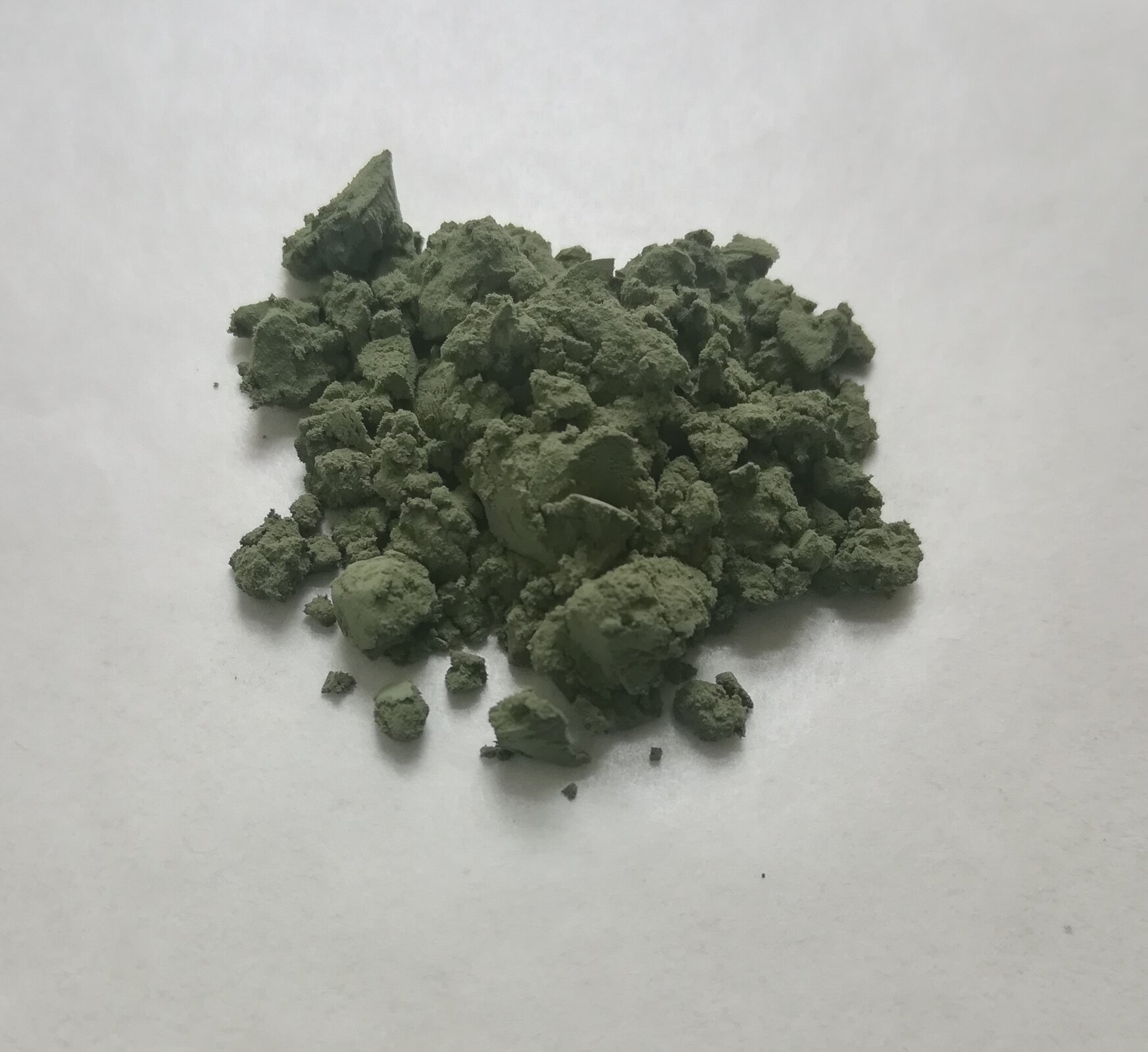 Zdjęcie przedstawiające tlenek manganu(II) w postaci zbrylonego ciemnozielonego proszku.