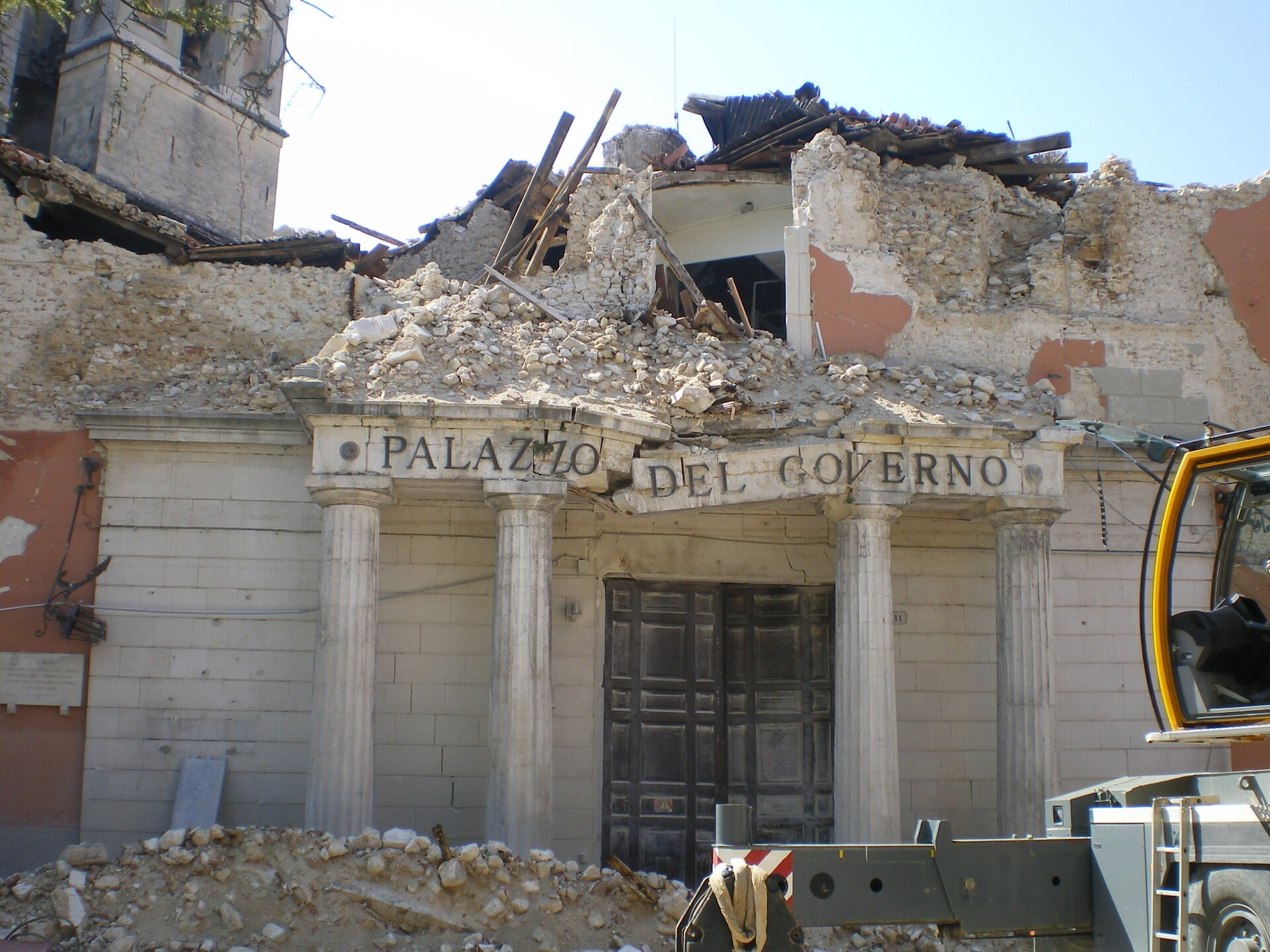 Na zdjęciu zawalony budynek, ocalał parter, przed budynkiem zwały gruzu.