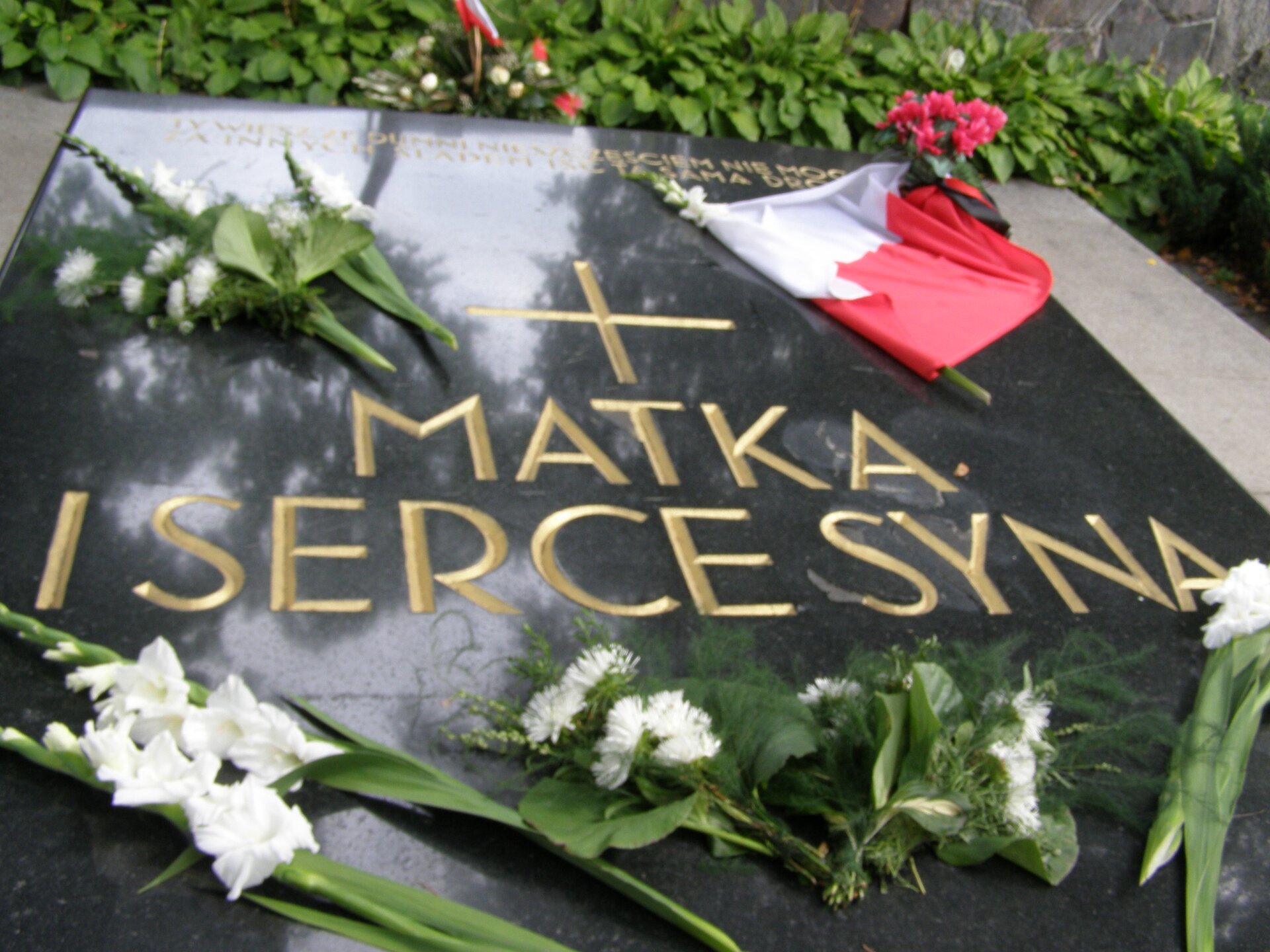 Fotografia barwna przedstawiająca ciemny nagrobek. na nim napis: "Matka. I serce syna".