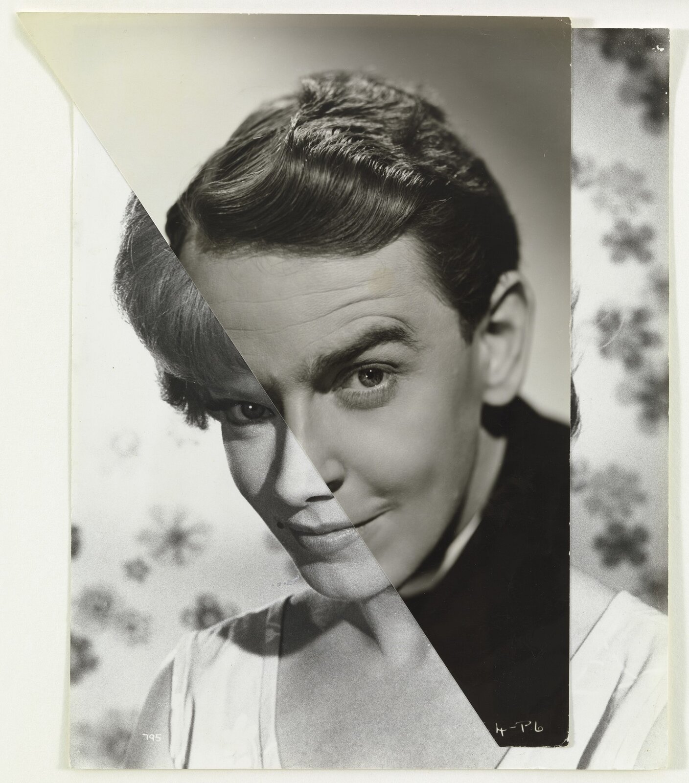 Ilustracja przedstawia dwa nałożone na siebie czarno‑białe zdjęcia kobiety i mężczyzny. Oba portrety przedstawiają młode osoby – ubrana na biało kobieta ma krótkie włosy i lekki uśmiech, a na jej czoło opada grzywka. Jej twarz pochylona jest lekko do przodu, oczy umalowane, a spojrzenie pewne. Mężczyzna ma krótkie włosy i lekki uśmiech, a przez uniesioną brew na jego czole widoczne są poziome zmarszczki. Ubrany jest na czarno. Fotografie nałożono na siebie w taki sposób, że usta i nosy obu osób łączą się, tworząc efekt podobieństwa. Tła różnią się – kobietę sfotografowano na białym tle z elementami kwiatowymi, a mężczyznę na tle jasnej ściany. 