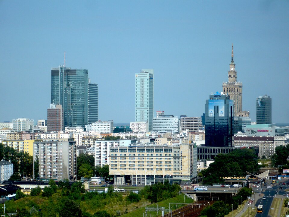 Panorama Śródmieścia Południowego w Warszawie z wysokości 16 pięter, pokazująca wieżowce biurowe (Warta Tower, Rondo 1, InterContinental), Pałac Kultury i Nauki w oddali oraz hotele, z zachmurzonym niebem i miejskim krajobrazem Woli