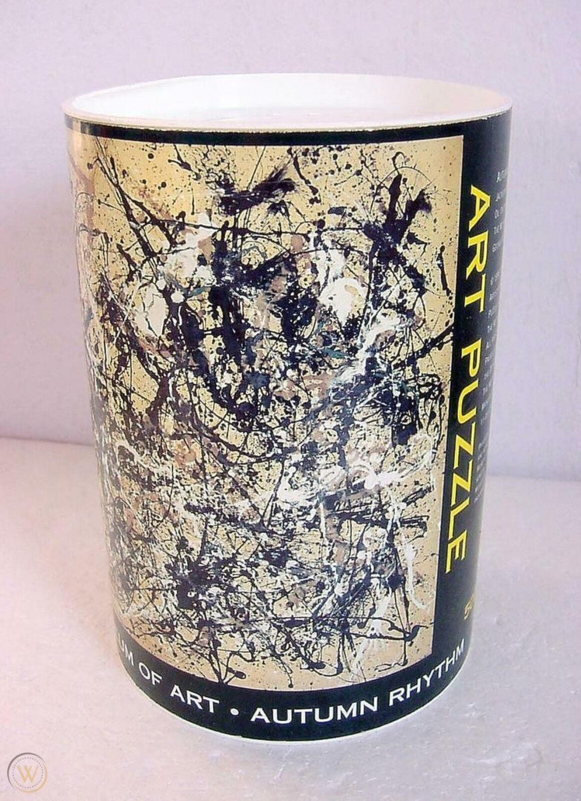 Zdjęcie przedstawia opakowanie puzzli ukazujących obraz Jacksona Pollocka pod tytułem „Rytm jesieni (numer 30)”. Opakowanie umieszczone centralnie na zdjęciu jest w kształcie tuby z białą pokrywką. Na pudełku znajduje się obraz wykonany w stylu abstrakcyjnym, składający się z plątaniny wielu nieregularnych linii różnej grubości, nachodzących na siebie. Linie są w kolorze czarnym, białym i brązowym na jasnobrązowym tle. Z prawej strony opakowania znajduje się żółty napis „Art Puzzle” umieszczony na czarnym tle. Na dole tuby jest biały napis „Autumn rythm” na czarnym tle.