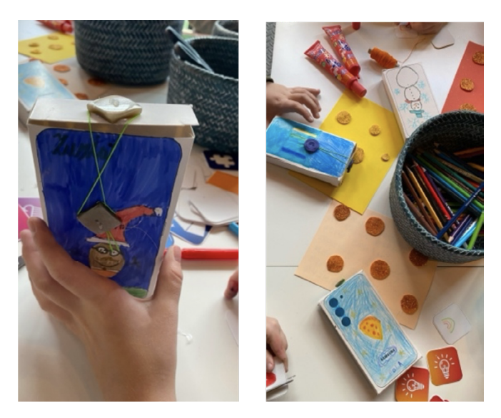 Zdjęcie pokazuje dziecięce ręce wykonujące prace plastyczne przy stole. Na pierwszym ujęciu widać kartonowe pudełko udekorowane rysunkiem postaci i kolorowym tłem, trzymane w dłoni dziecka. Na drugim ujęciu na stole leżą różne materiały: kolorowe kredki w koszyczku, tubki z farbami, naklejki i inne ozdoby. Na kilku kartonowych pudełkach dzieci narysowały kosmiczne motywy, takie jak planety i gwiazdy. Cała scena przedstawia kreatywną zabawę i tworzenie własnych projektów.