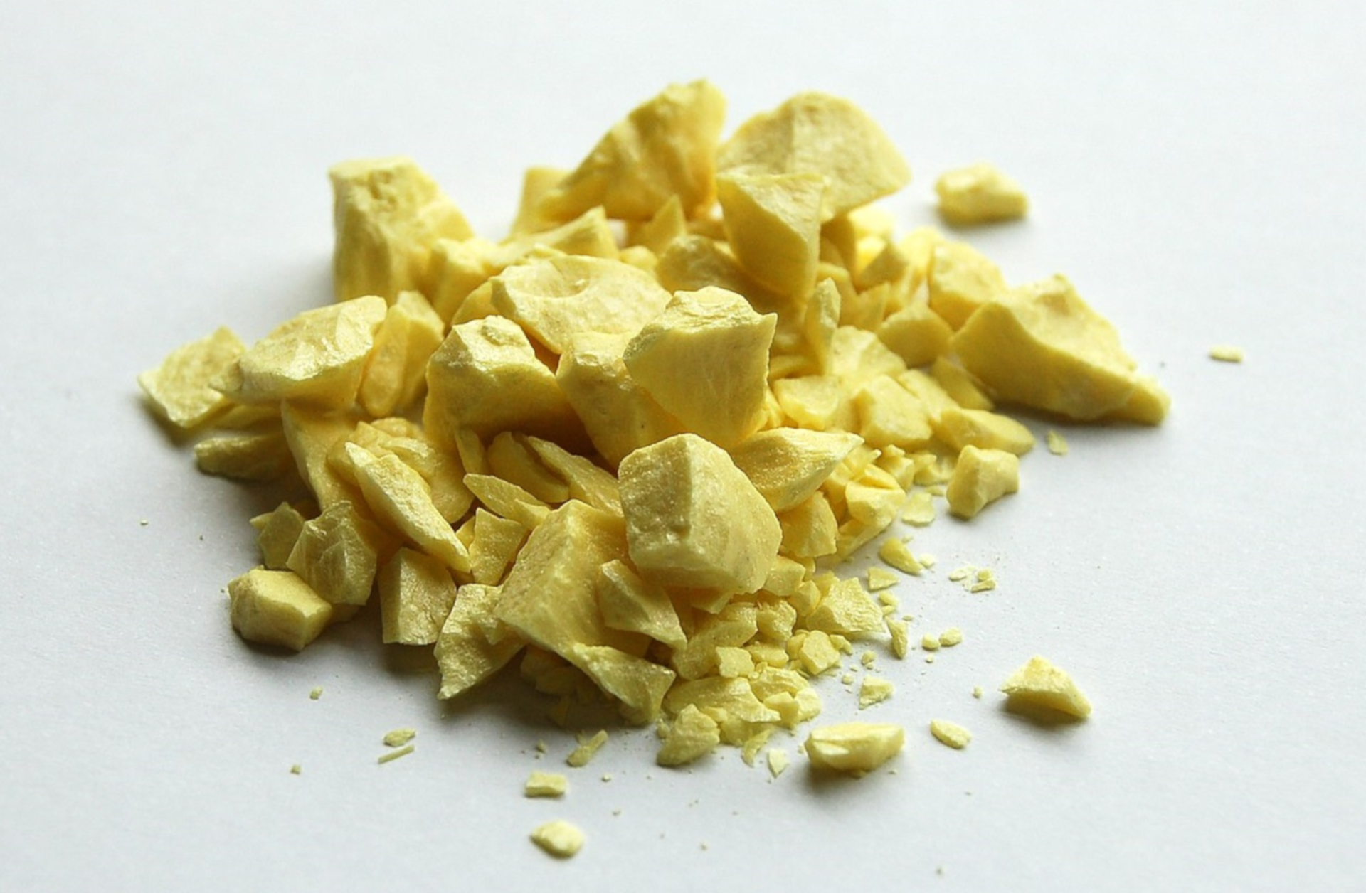 Na ilustracji ukazano stosik drobnych, jasnożółtych skruszonych skał na białej powierzchni.