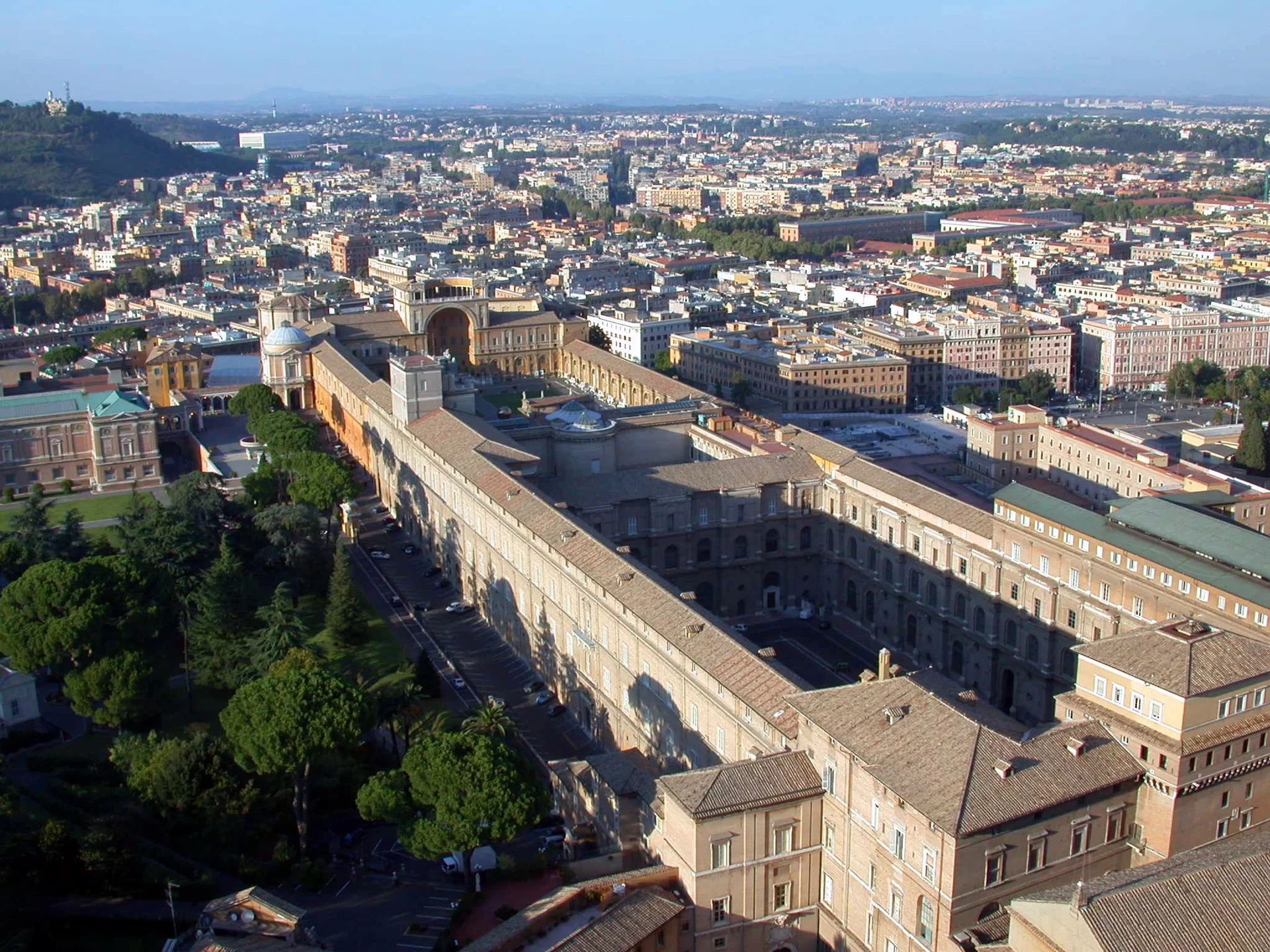 Zdjęcie zostało wykonane z lotu ptaka i przedstawia państwo Watykan oraz kompleks budynków zbudowanych w stylu renesansowym, należących do Muzeów Watykańskich. Budynki Muzeów zostały wykonane z pomarańczowej cegły, dachy pokryte zostały dachówkami w kolorach: brązowym,  i szarym. Obok Muzeów (z lewej strony) znajduje się park oraz rosnące drzewa.