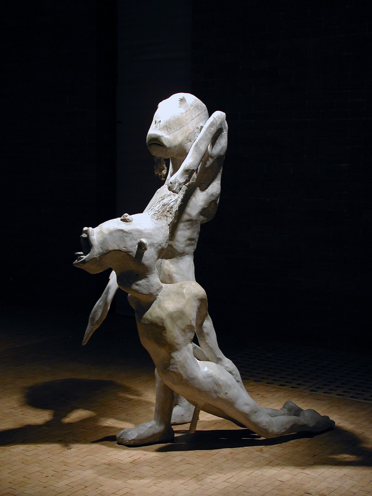 Zdjęcie przedstawia rzeźbę pod tytułem: „Ofiara Izaaka”, autorstwa Sylwestra Ambroziaka. Kompozycja przedstawia dwie postacie, najprawdopodobniej są to mężczyźni. Głowy mężczyzn są podłużne oraz zniekształcone. Jedna z nich ma krzyczący wyraz twarzy, ma pozycję półleżącą. Druga postać, ma pozycję dominującą nad pierwszą postacią, o czym świadczy ułożenie jego ciała.  Jego ręka jest uniesiona. Mężczyzna ciągnie za włosy postać leżącą. Tło jest koloru czarnego.