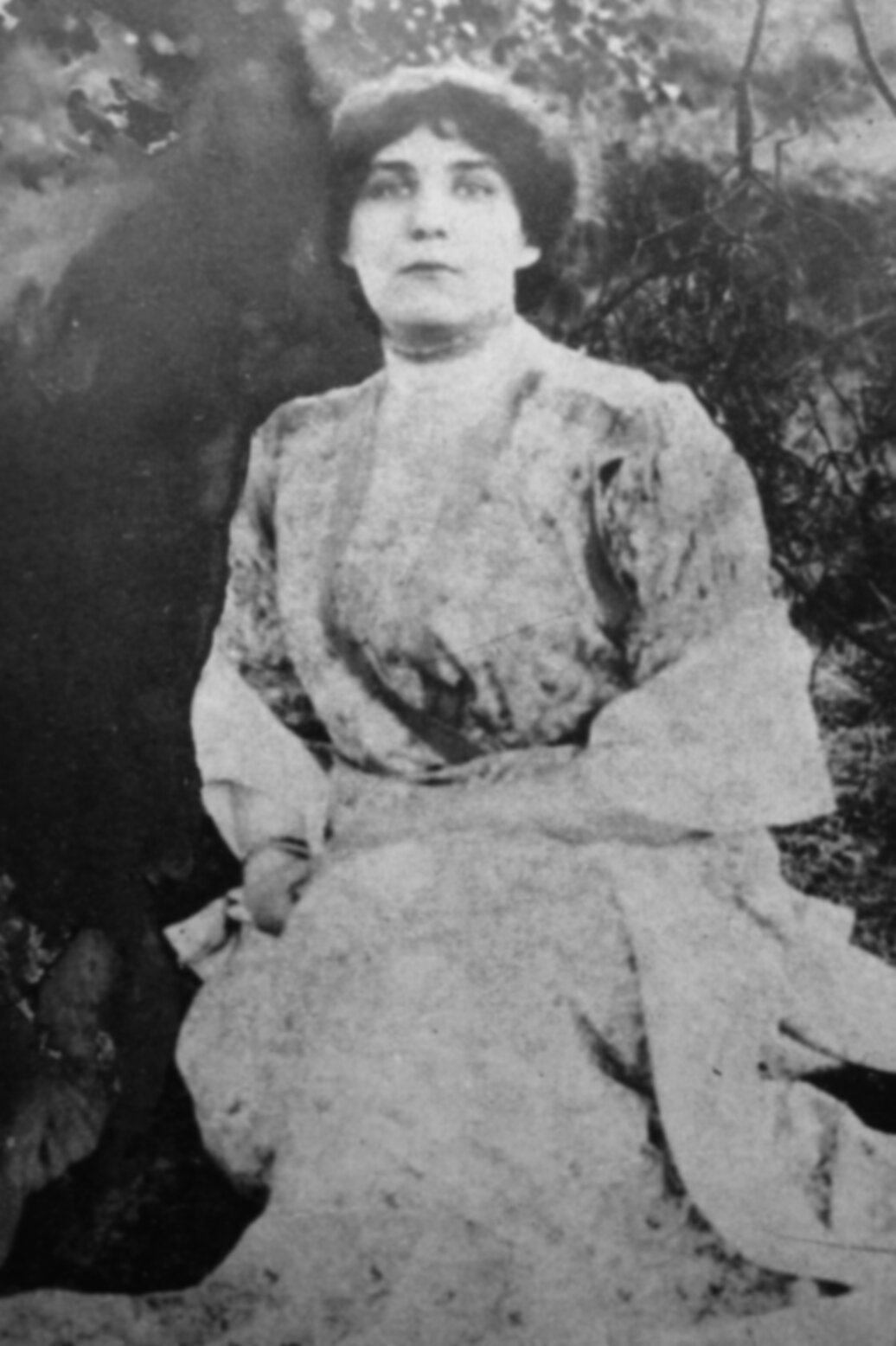 Zdjęcie przedstawia Zofię Nałkowską w pozycji siedzącej. Ma ciemne, upięte z tyłu głowy włosy. Ubrana jest w jasną sukienkę. Tło jest ciemne, niewyraźne.