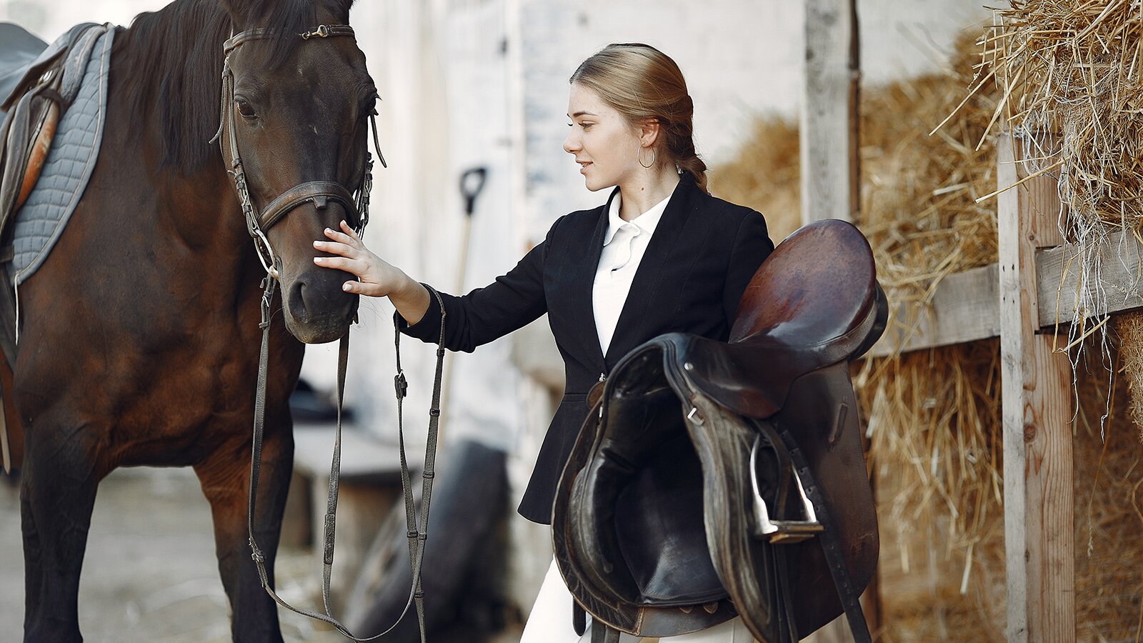 Zdjęcie przedstawia kobietę w młodym wieku trzymającą w lewej dłoni sidło. Prawą ręką głaszcze pysk konia. 