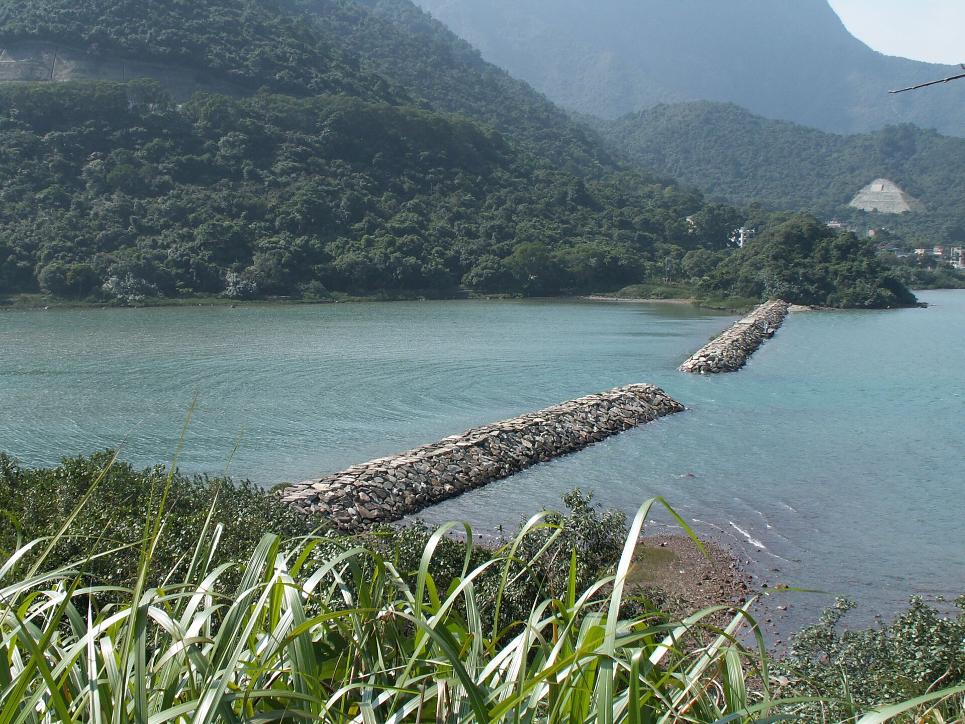 Rys. 1. Zdjęcie poglądowe przedstawia zatokę oddzieloną od morza kamiennym falochronem. Pośrodku falochronu jest wąska przerwa, przez którą przechodzą fale morskie. Za falochronem fale rozchodzą się w postaci okręgów, których środki leżą w szczelinie falochronu.