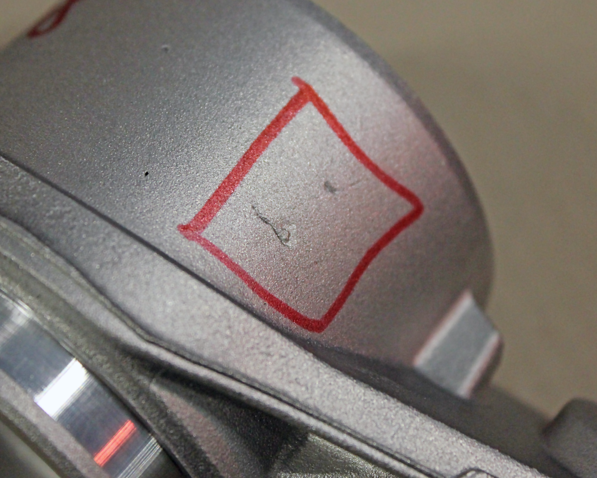 Zdjęcie przedstawia przybliżony, walcowaty, metalowy element. Ma on niedolew, czyli ubytek na powierzchni. Ten niedolew jest zaznaczony w czerwonym kwadracie.