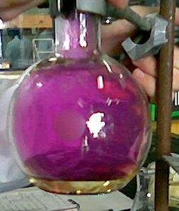 Zdjęcie przedstawia szklaną kolbkę wypełnioną fioletowym gazem. Kolba umieszczona jest na statywie, którego fragment widać na fotografii.