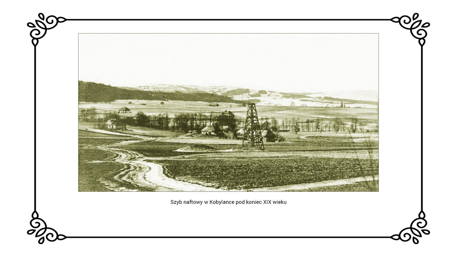 Slajd przedstawia ilustrację z terenu Kobylanki koło Gorlic, gdzie w centralnej części obrazu, na polu, wzniesiono szyb naftowy. Wieś jest w oddaleniu od pól i prowadzi do niej bita droga usytuowana po lewej stroni obrazu. W oddali widać obszar jest pagórkowaty i częściowo zalesiony.