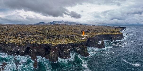 Zdjęcie lotnicze wybrzeża o wysokości kilkudziesięciu metrów. Ściany są bardzo strome, niemal pionowe, składają się ze skał. U podnóża wzburzone morze. U góry płaski teren pokryty roślinnością, latarnia morska.