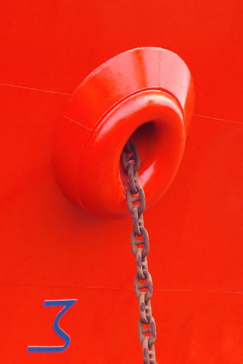 Zdjęcie przedstawia kluzę kotwiczną. Widać otwór w burcie, przez który przechodzi łańcuch.