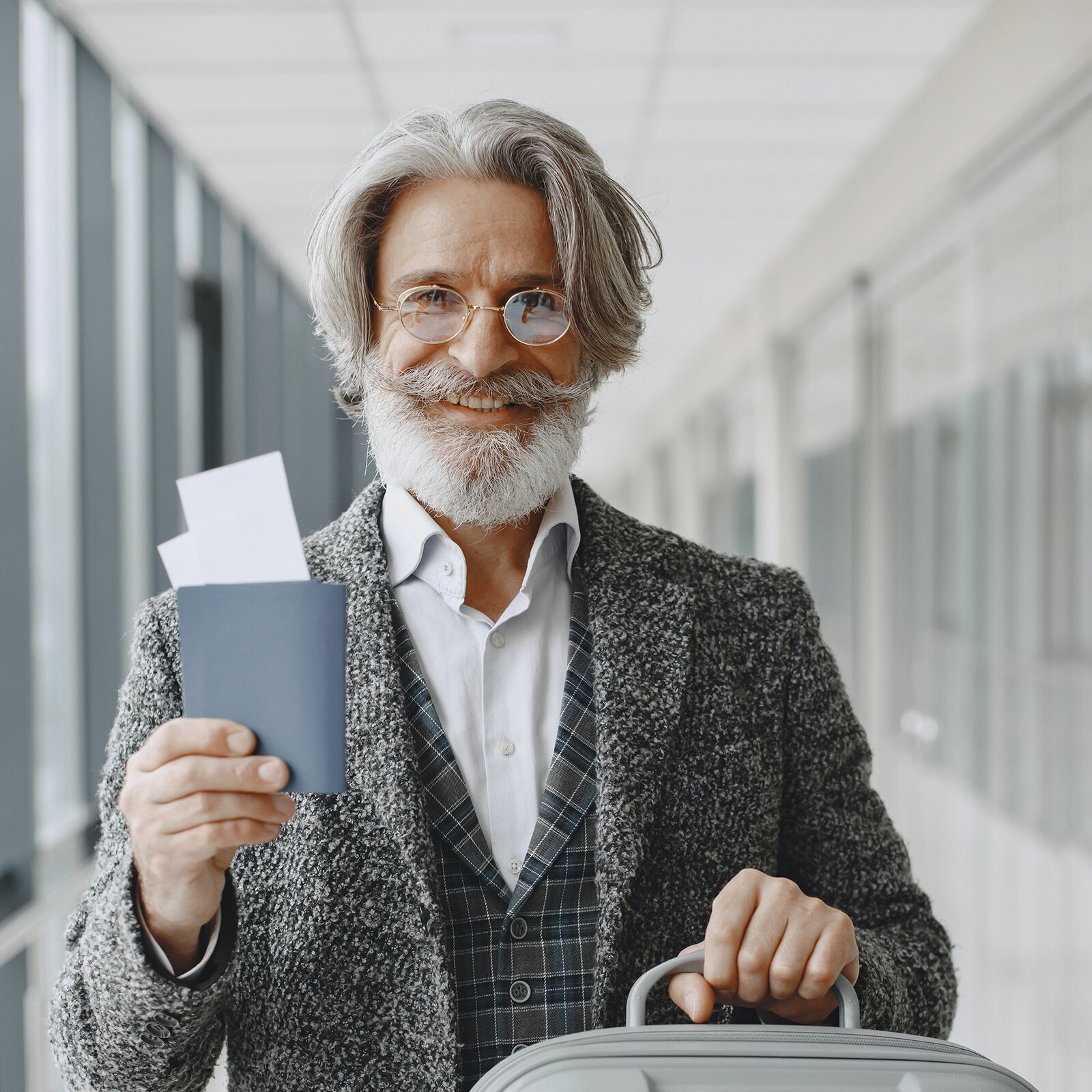 Zdjęcie przedstawia starszego, uśmiechniętego mężczyznę. Ma zmarszczki i dłuższe, proste, siwe włosy. Nosi brodę i wąsy. Ma okulary korekcyjne. Jest ubrany w koszulę i płaszcz, a w ręce trzyma dokumenty.