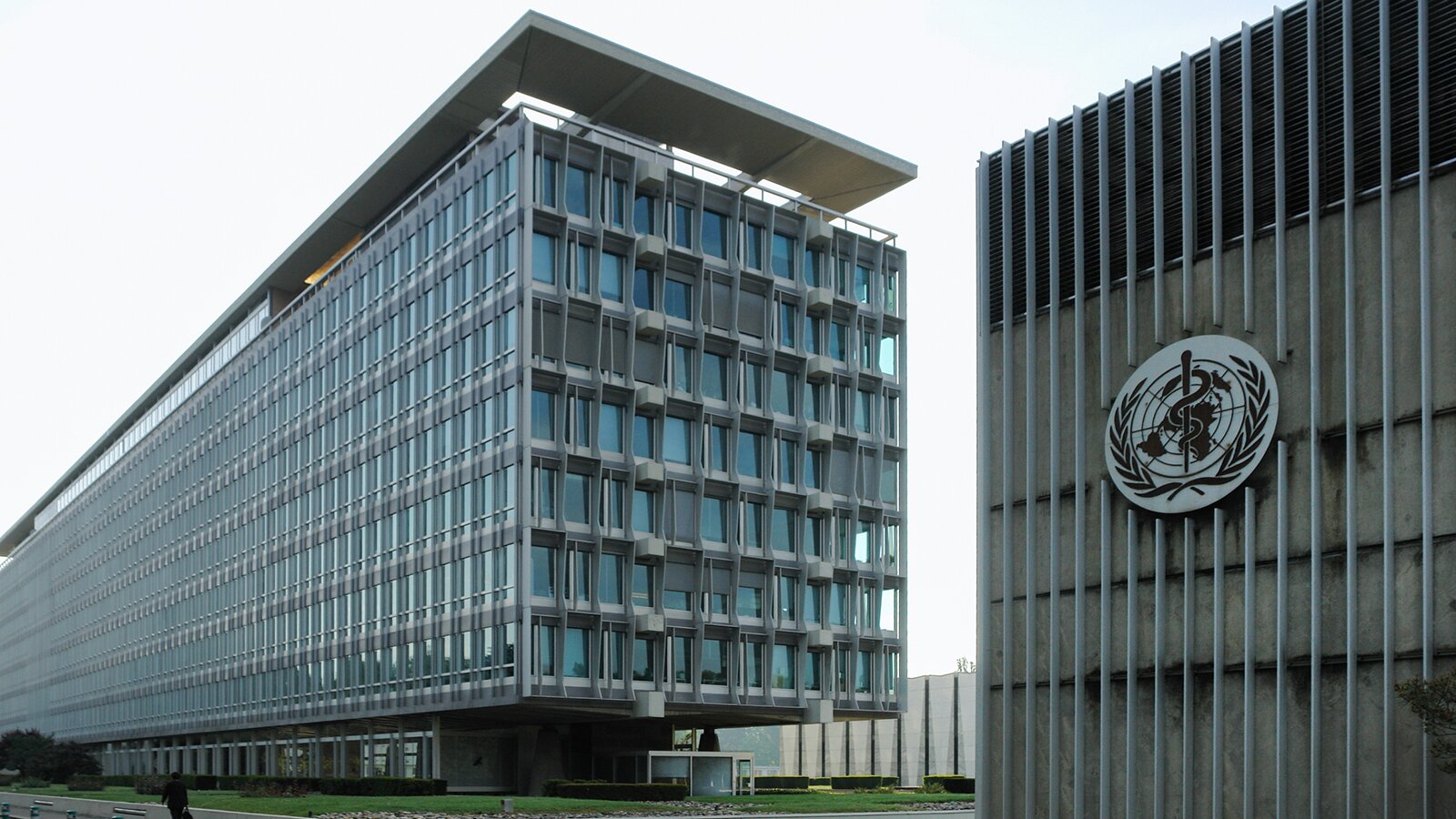 Zdjęcie przedstawia dwa budynki. Po prawej stronie widoczny jest wysoki budynek, na froncie którego widoczne jest logo. Logo przedstawia mapę świata z poszczególnymi kontynentami, oglądaną z czterdziestego równoleżnika szerokości południowej, na setnym stopniu szerokości zachodniej od Greenwich. Mapa otoczona jest dwiema gałązkami oliwnymi. Pośrodku widoczny laska Asklepiosa – symbol medycyny i sztuki lekarskie przedstawiony w formie węża wijącego się wokół prostej laski. Na lewo widoczny jest siedmiokondygnacyjny, przeszklony budynek.