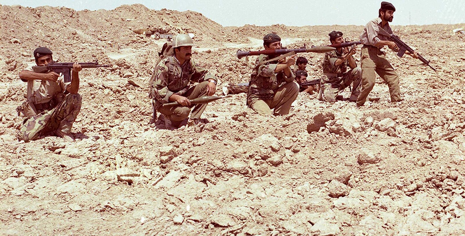 Zdjęcie przedstawia grupę uzbrojonych żołnierzy przygotowujących się do ostrzału. Dookoła jałowy, niezamieszkany teren.