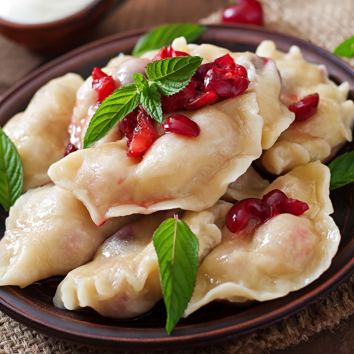 Zdjęcie przedstawia pierogi wyłożone na talerzu ozdobione listkami mięty .