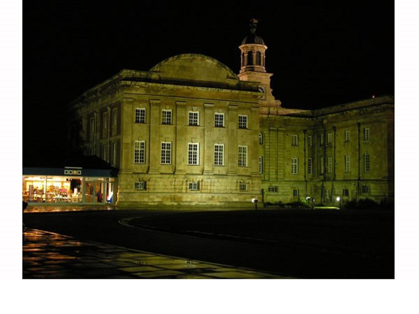 Na zdjęciu jest podświetlony budynek. Przed nim jest czarny plac. Fotografia jest zrobiona w nocy.