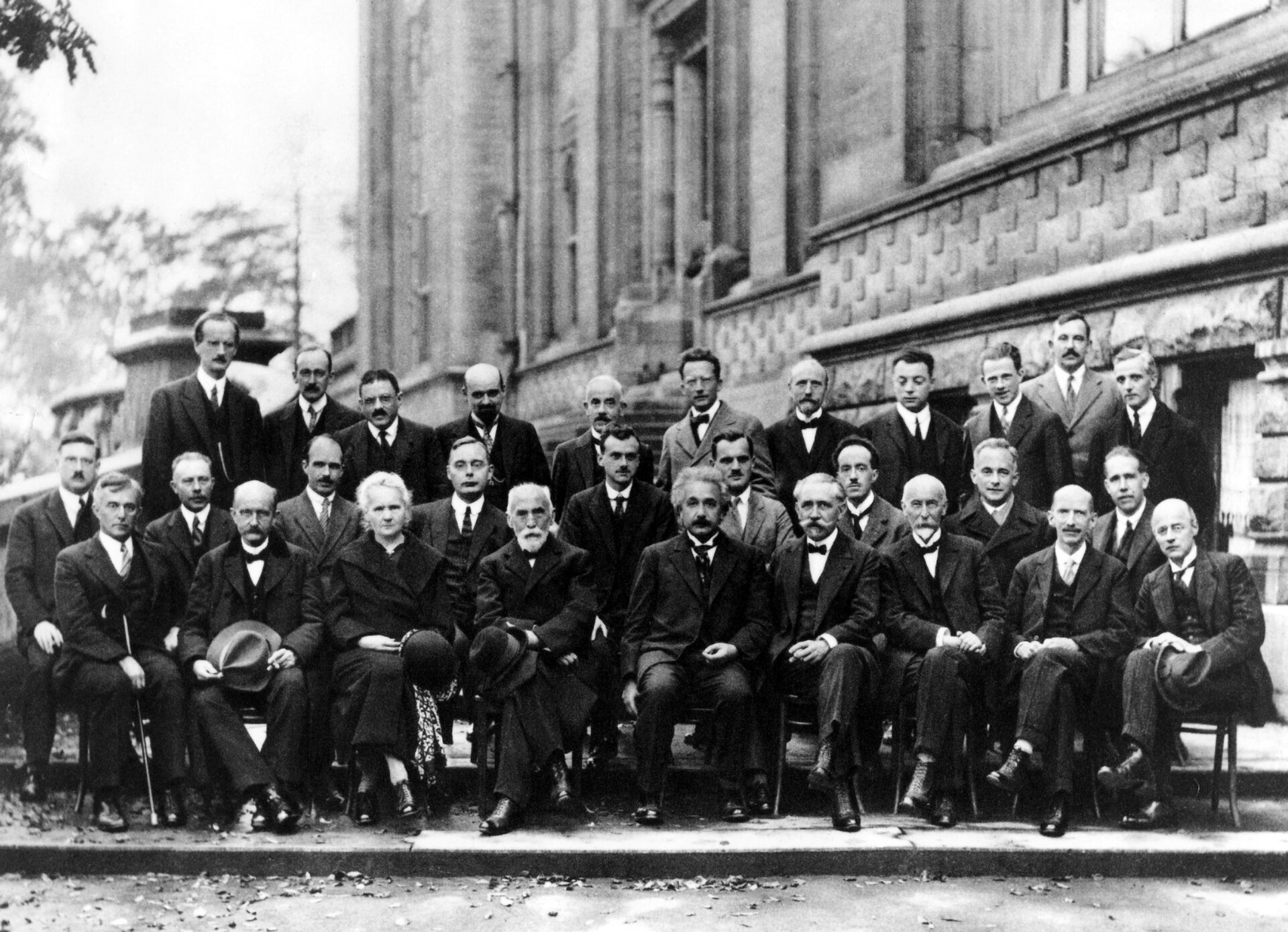 Rys. b. Zdjęcie poglądowe przedstawia pozowane ujęcie grupy naukowców. Kilkunastu naukowców siedzi na krzesłach, kilkunastu stoi za nimi. Grupę stanowią mężczyźni i jedna kobieta.