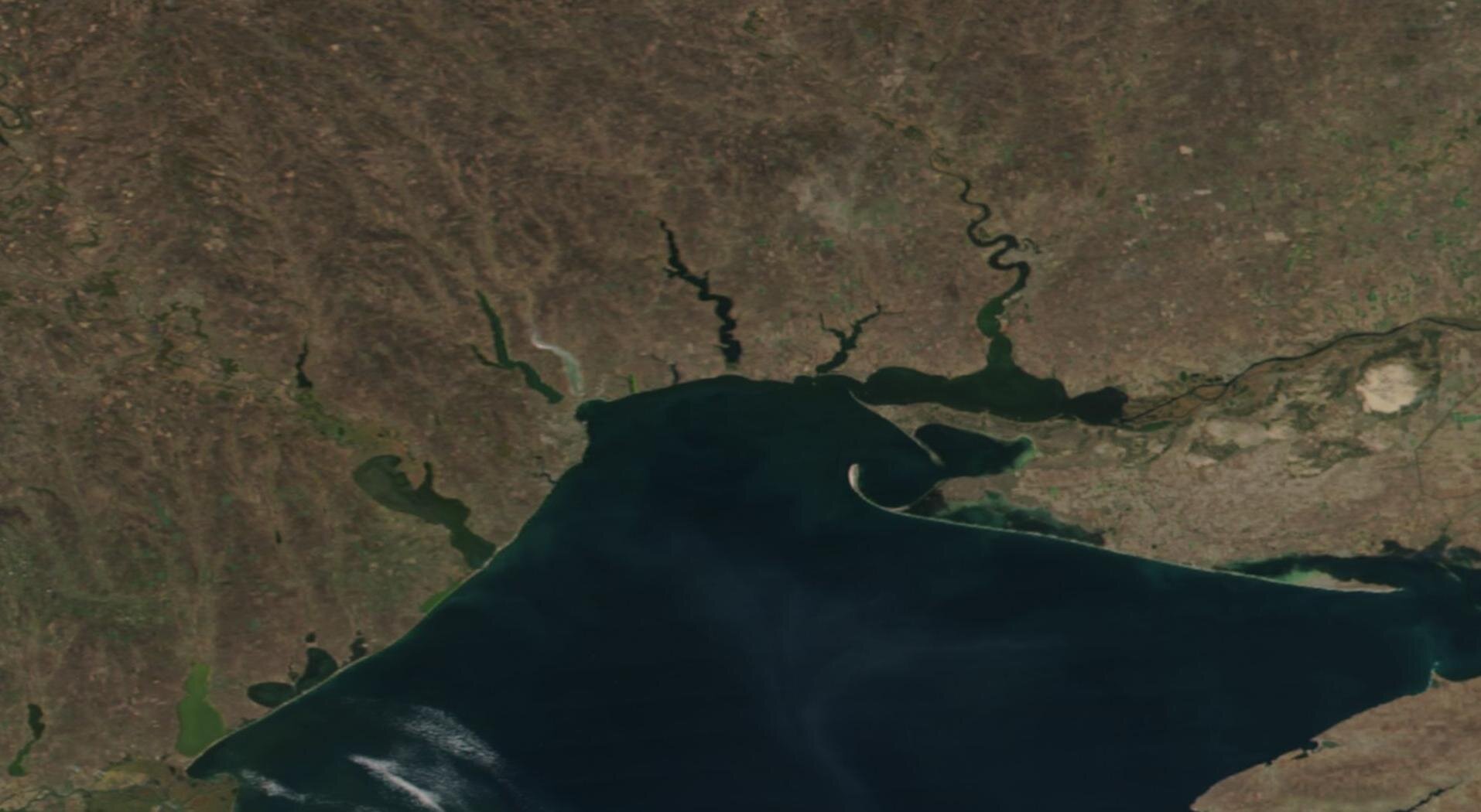 Zdjęcie satelitarne przedstawia fragment wybrzeża. W głąb lądu wchodzą krótkie, wąskie zbiorniki wodne.