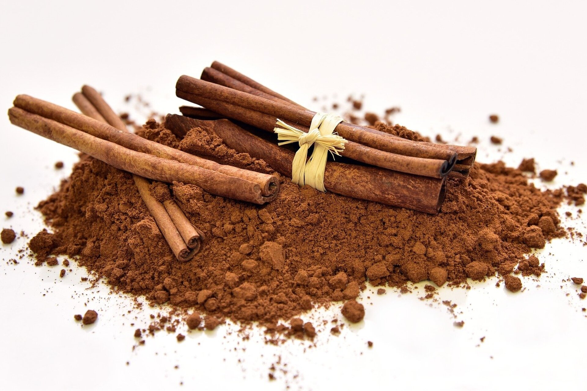 Zdjęcie przedstawia laski cynamonu leżące na cynamonie w proszku.