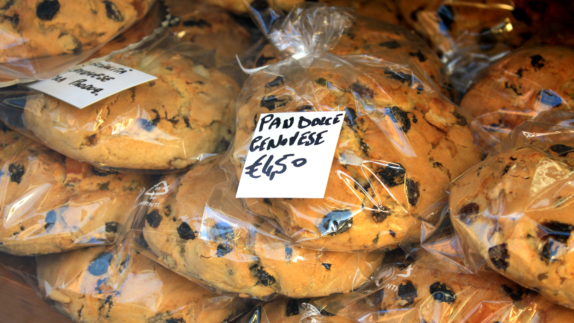 Zdjęcie przedstawia Pandolce, słodkie chlebki z suszonymi owocami. Chlebki zapakowane są w folię. Na zdjęciu widoczna jest także cena: Pandolce Genovese 4,50 euro.