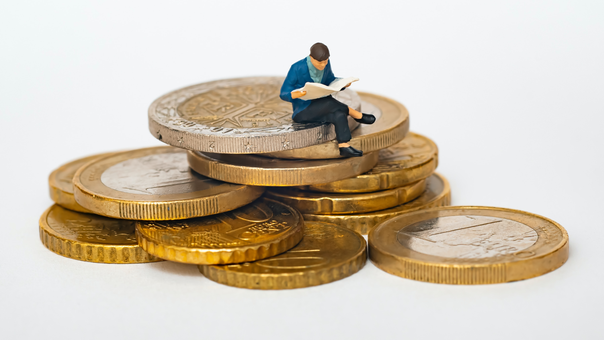 Na zdjęciu pokazany jest stos monet waluty euro. Na stosie znajduje się miniaturowa figurka siedzącego mężczyzny czytającego gazetę.