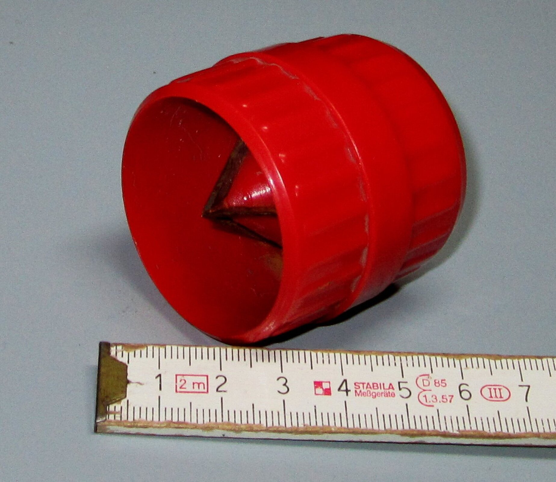 Ilustracja przedstawia niewielkie narzędzie wyglądem przypominające nakrętkę. Narzędzie ma okrągły kształt i wewnętrzny stożek, którym usuwa się materiał. Obok znajduje się miarka, by ukazać wielkość przyrządu.