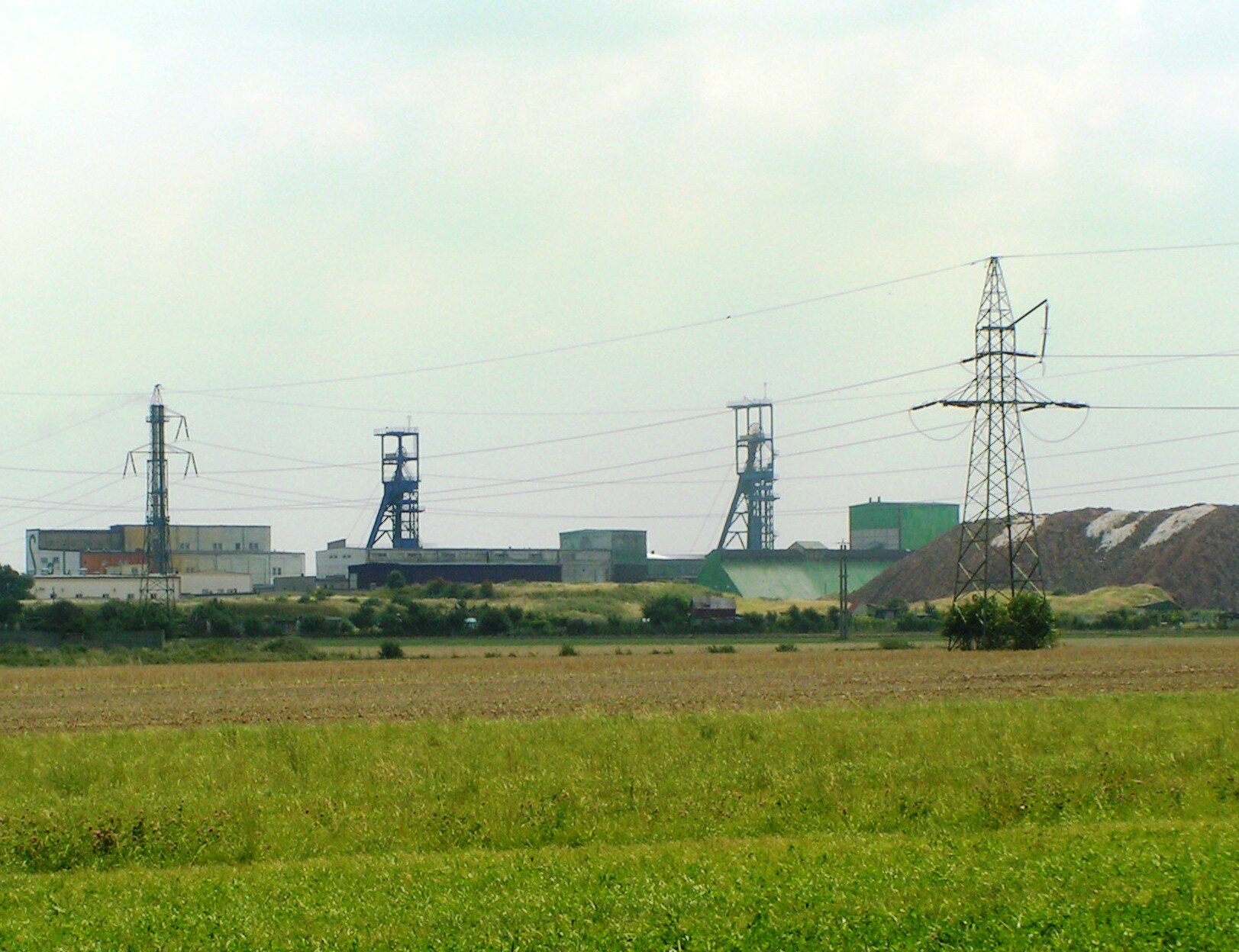 Zdjęcie ukazuje zabudowania kopalni soli w Kłodawie. Na terenie kopalni stoją dwa szyby służące do wydobycia soli. Na pierwszym planie są pola i łąki.